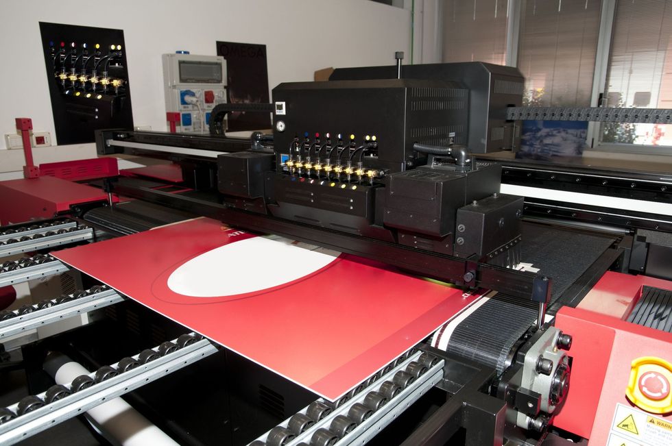 Large format printer printing a red and white design on a sheet of material.