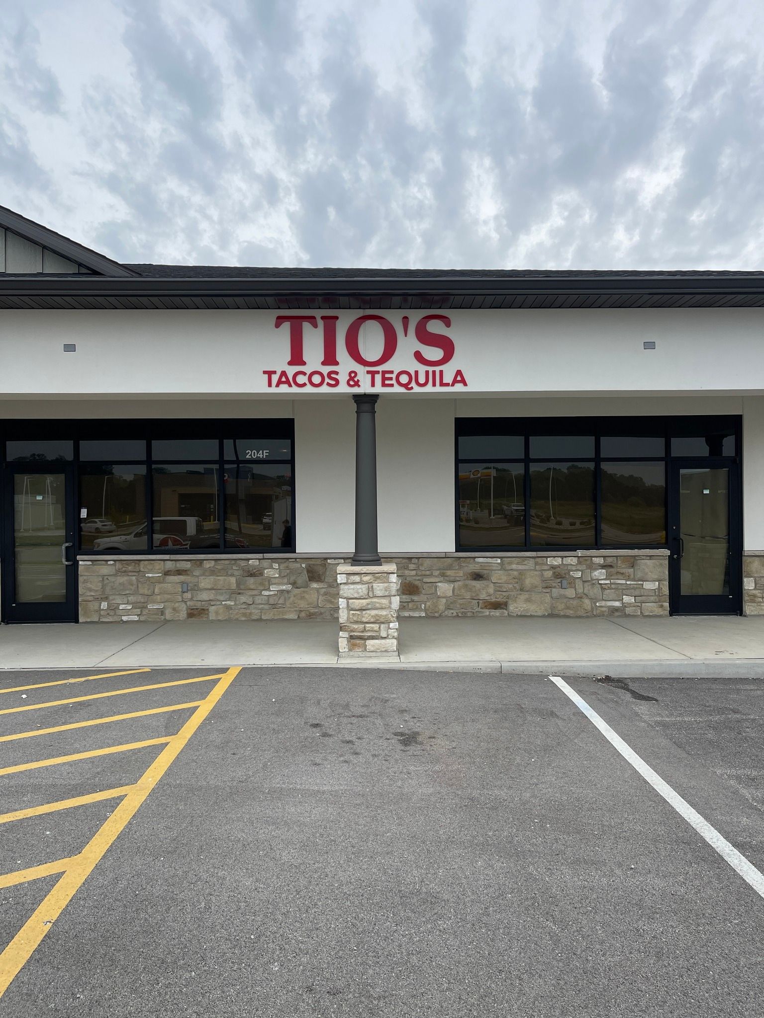 Tio's Tacos & Tequila restaurant exterior with red sign letters, black doors and windows, cloudy sky.