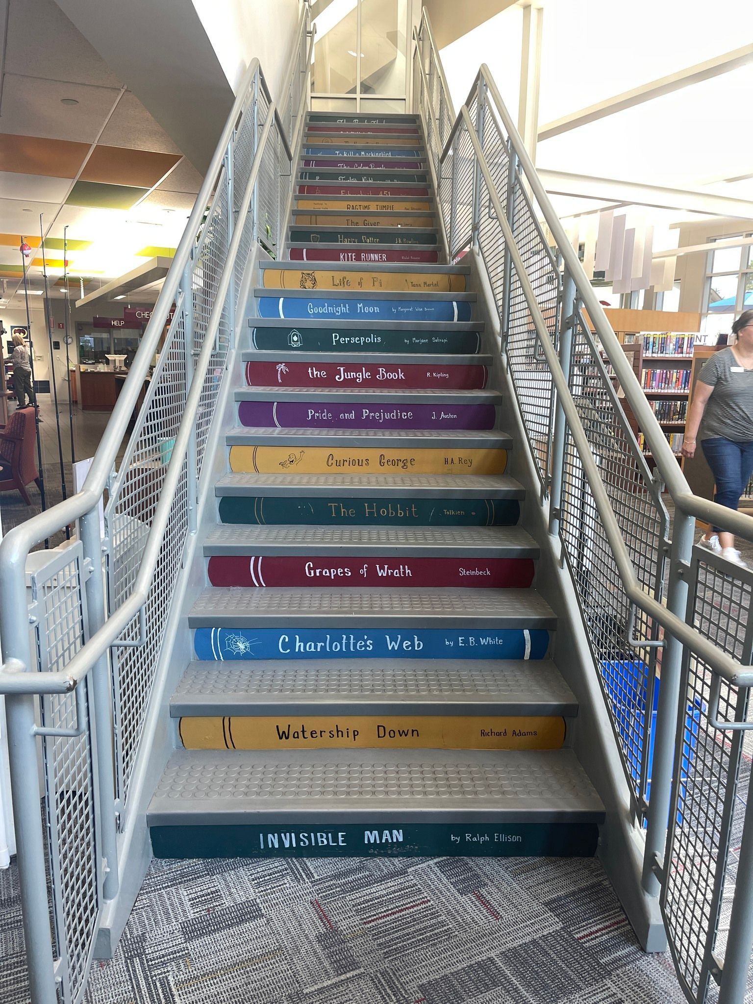 Staircase with colorful book-themed steps in a library, metal railing.