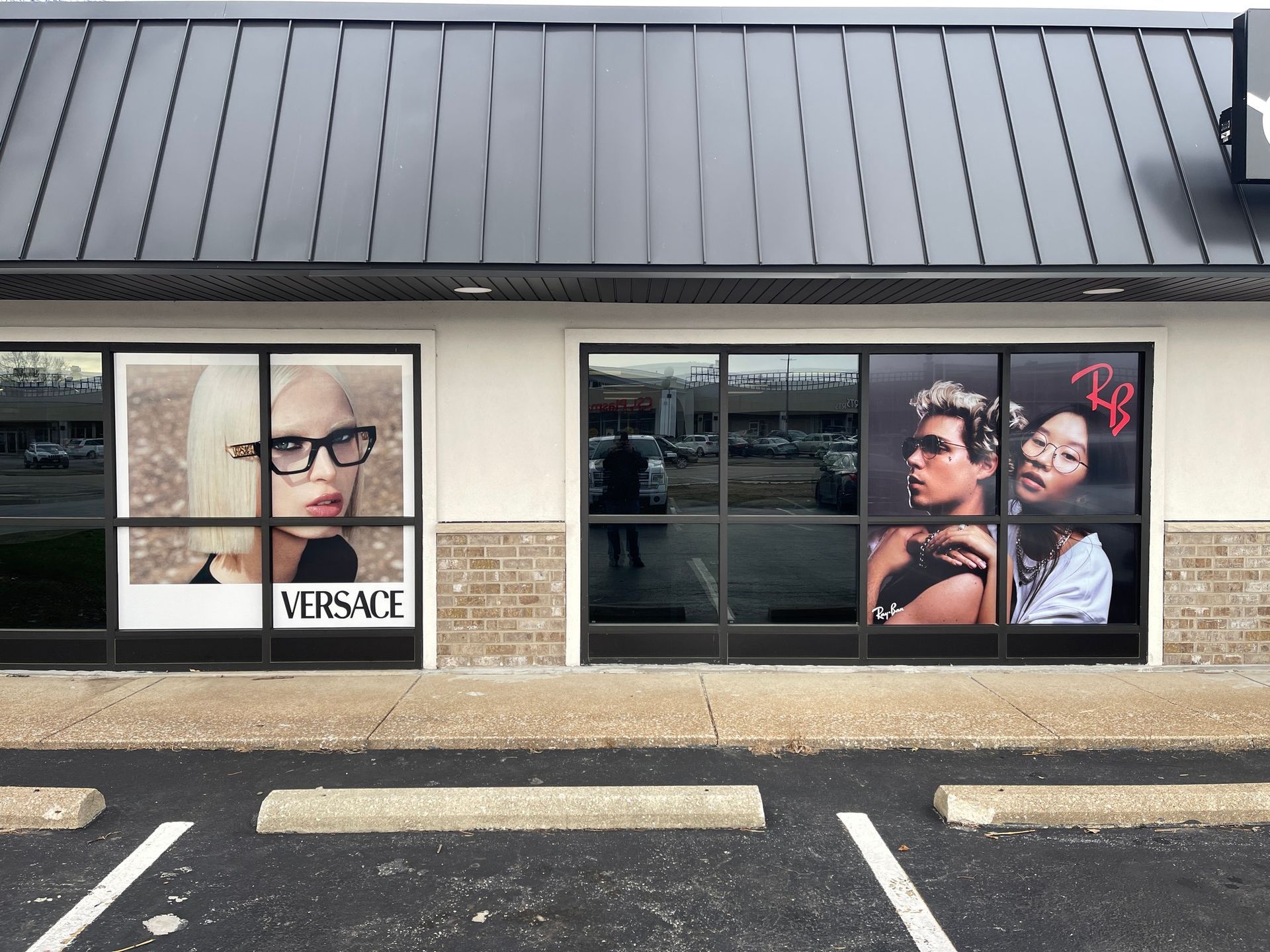 Storefront with black awning and large window displays advertising Versace glasses and Ray-Ban sunglasses.