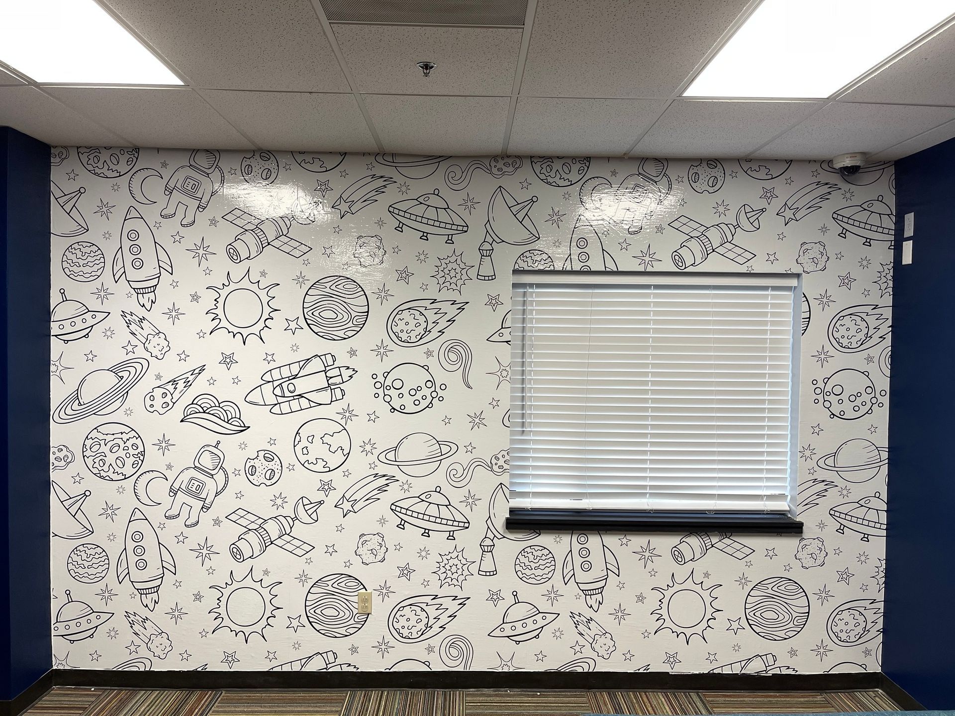 Wall with black and white space-themed doodles, a window with blinds, and blue painted trim.