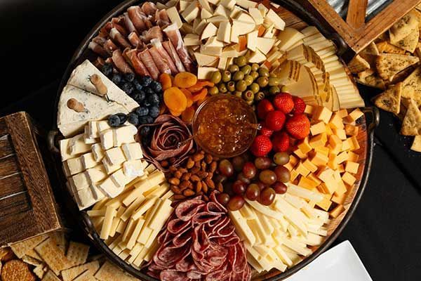 A large platter filled with cheese , fruit , nuts and crackers.