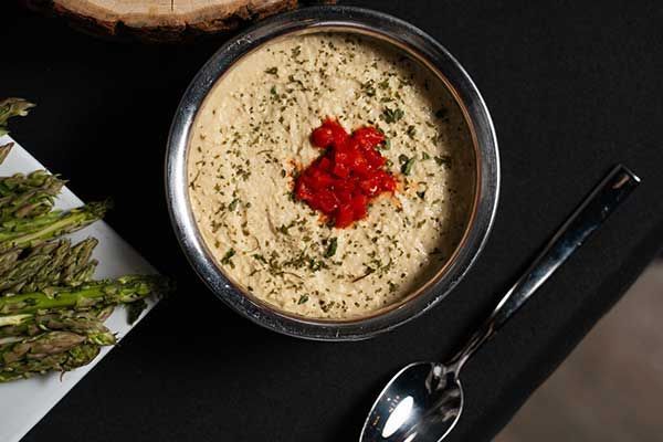 A bowl of food with a spoon on a table next to a plate of asparagus.