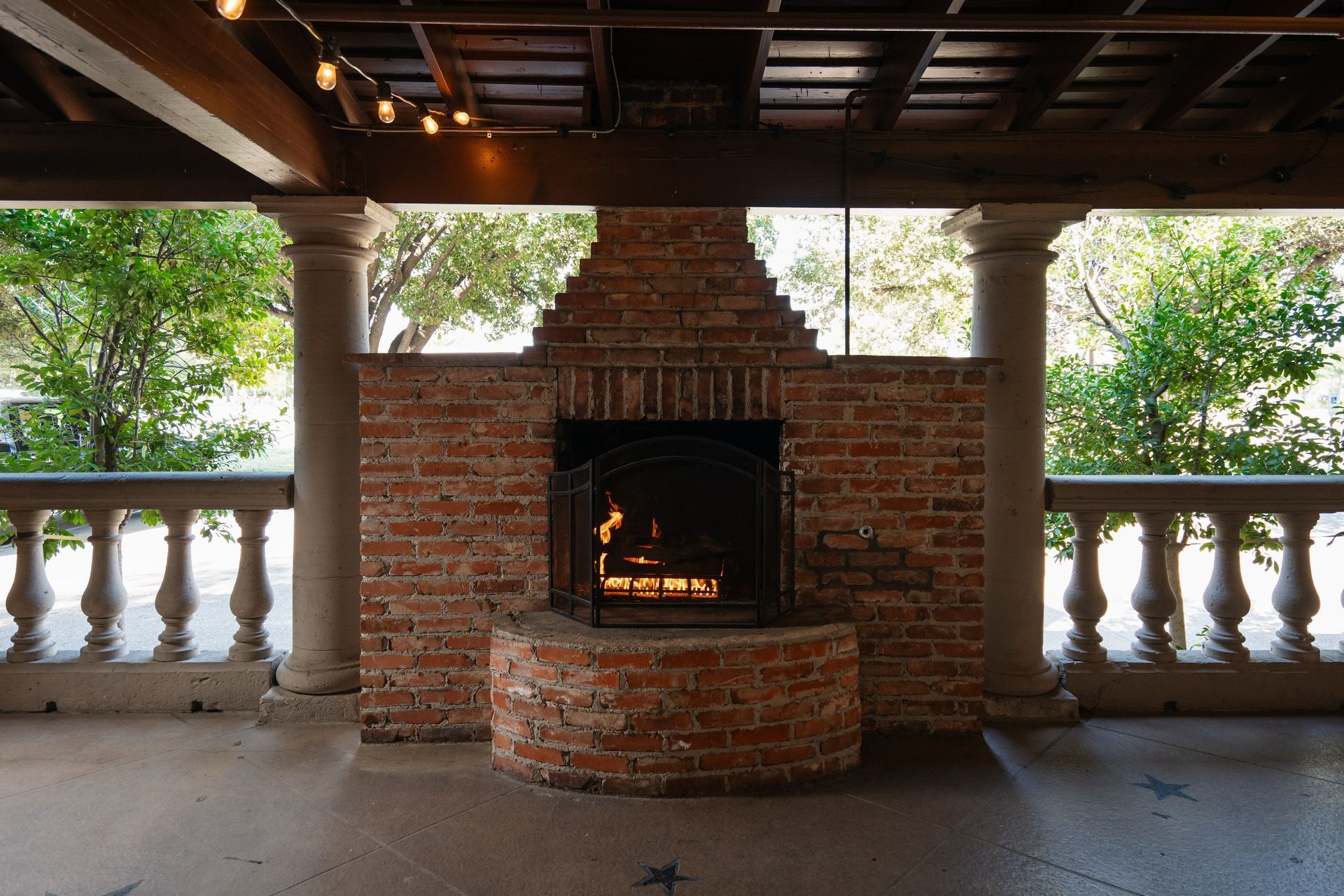 A brick fireplace is sitting on a porch with trees in the background