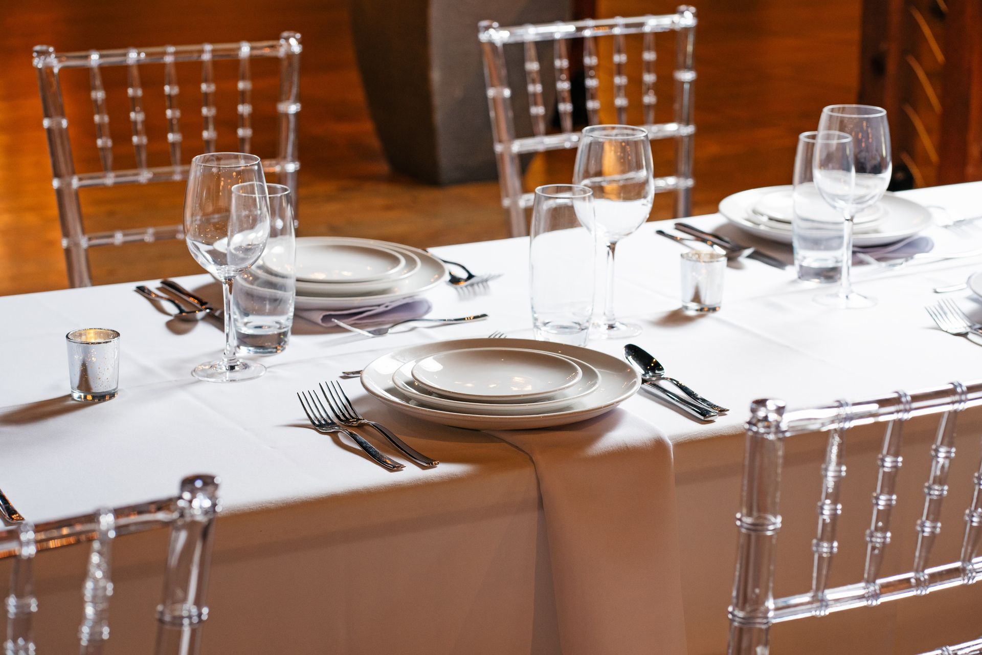 A table with clear chairs and plates and glasses on it