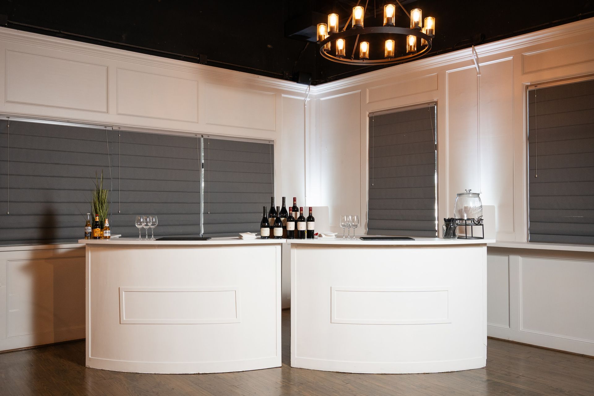 Two white bar tables in a room with bottles of wine on them.