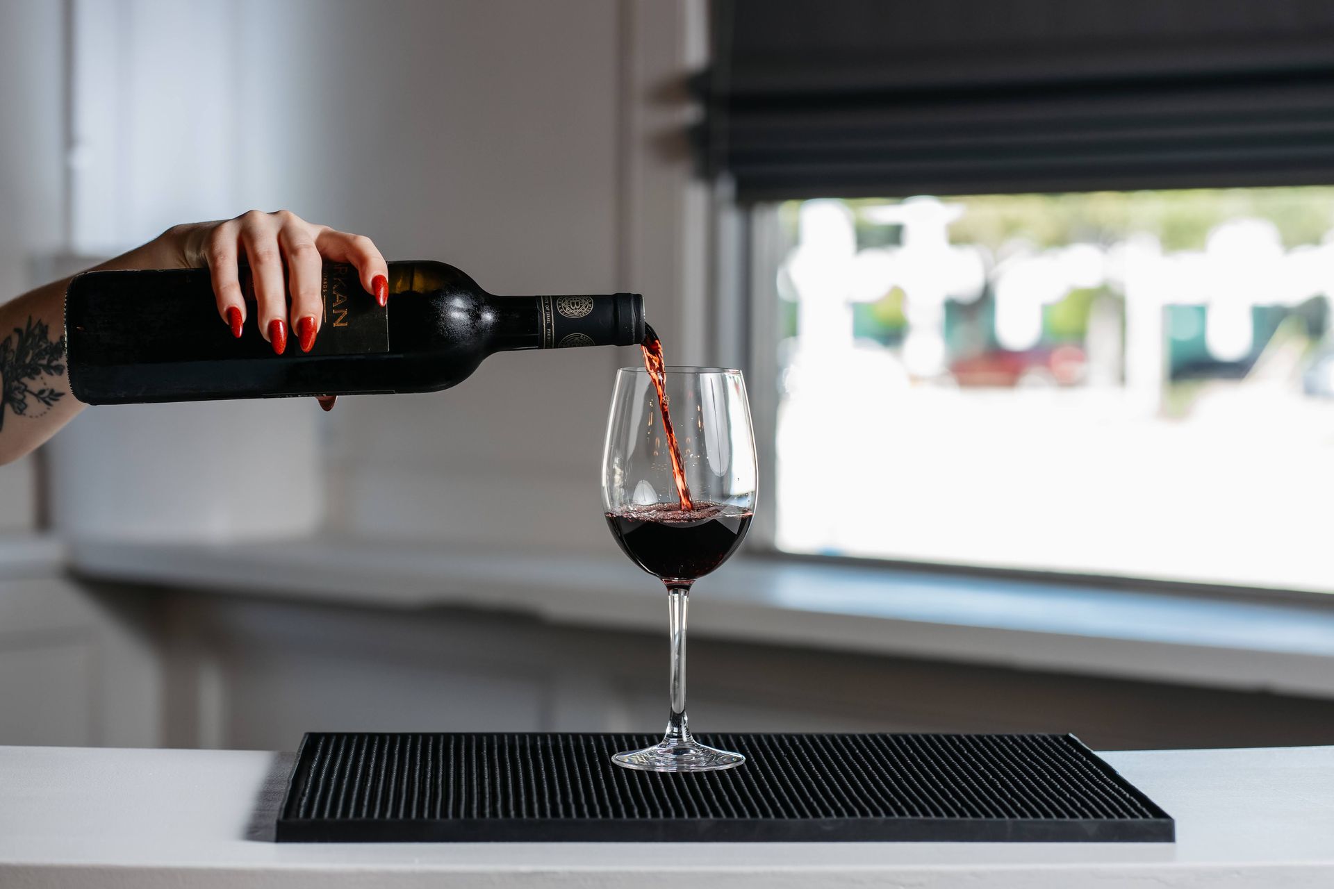 A woman is pouring red wine into a glass on a counter.