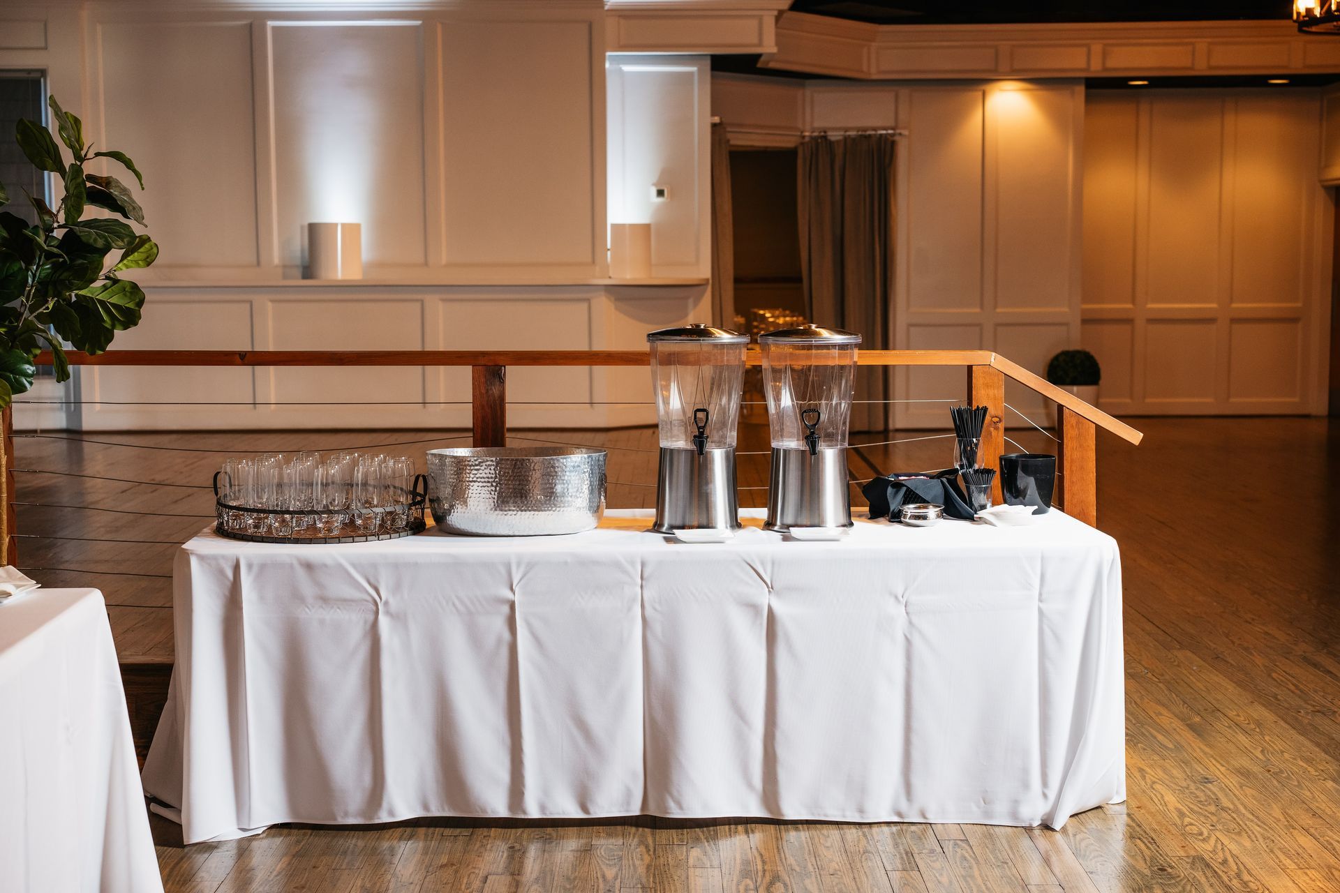 A table with a white tablecloth and a bunch of drink dispensers on it in a room.