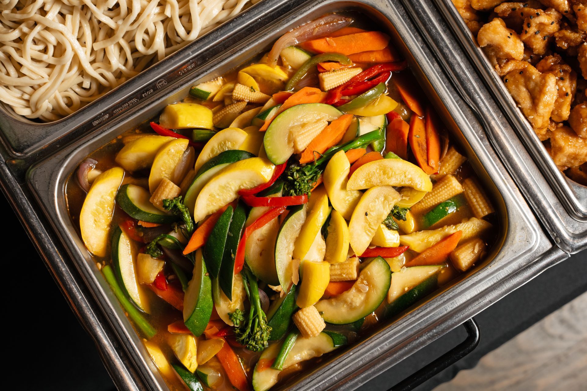 A buffet tray filled with vegetables and noodles.