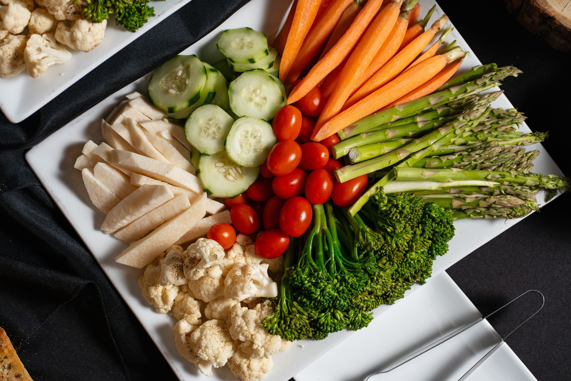 A white plate topped with carrots , cucumbers , tomatoes , broccoli and asparagus.