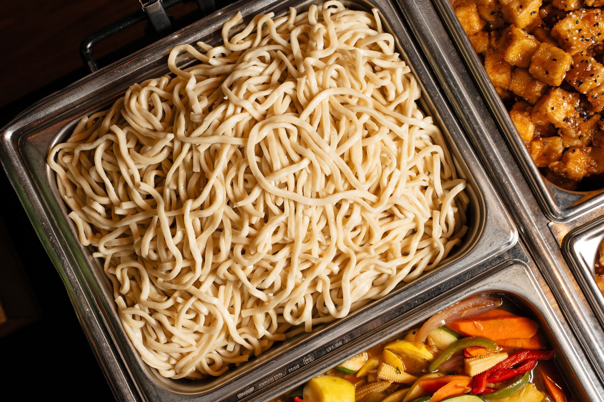 A buffet tray filled with noodles and vegetables.