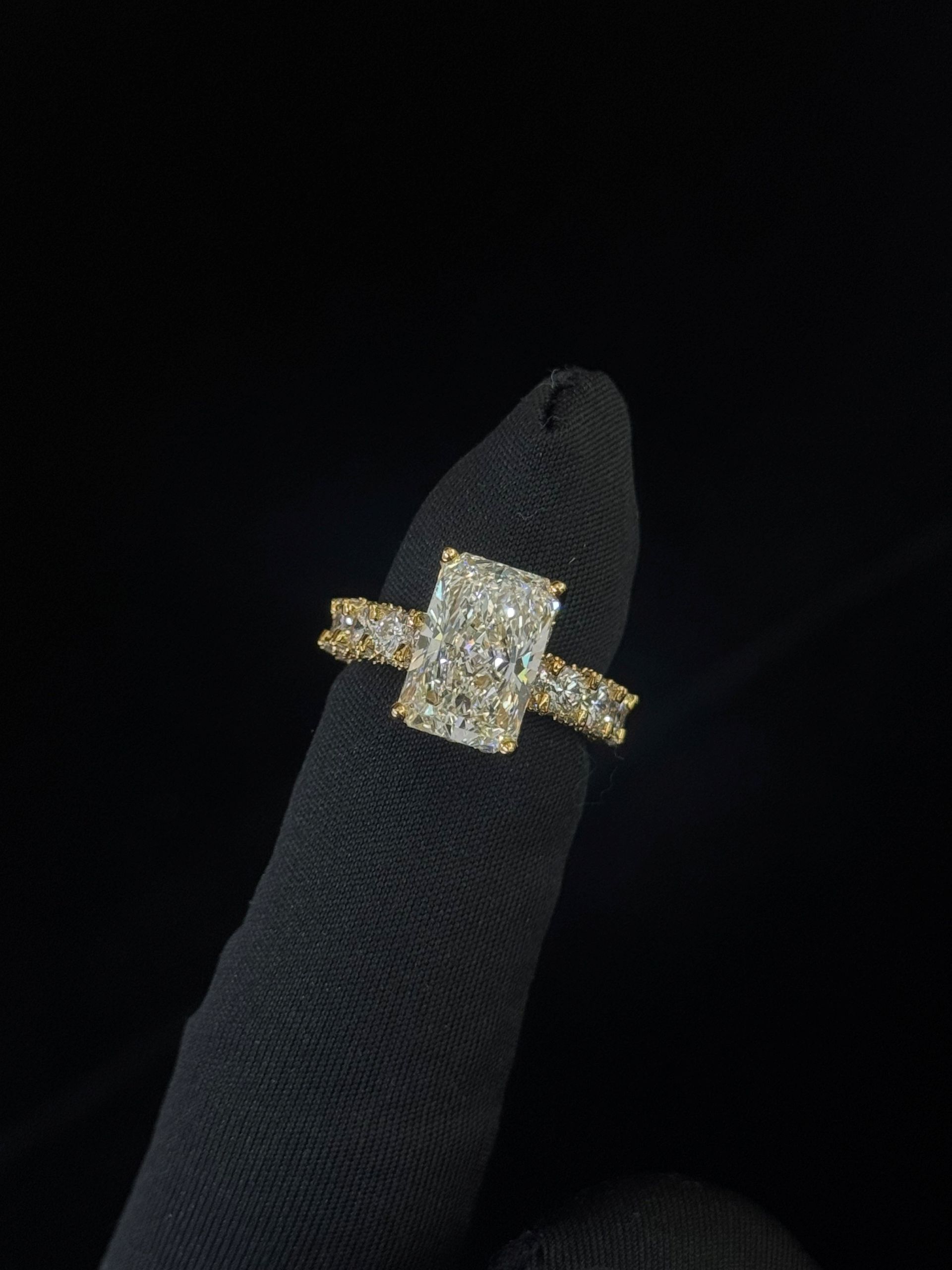 Gold ring with a rectangular center stone and diamond band on a black display stand