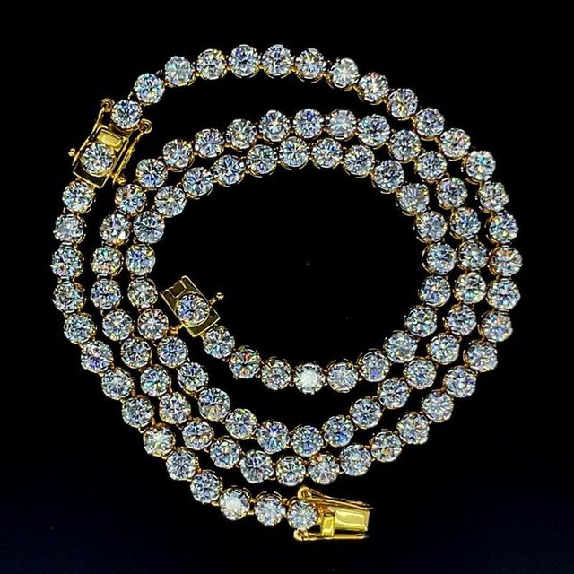 Gold diamond tennis necklace coiled on black background