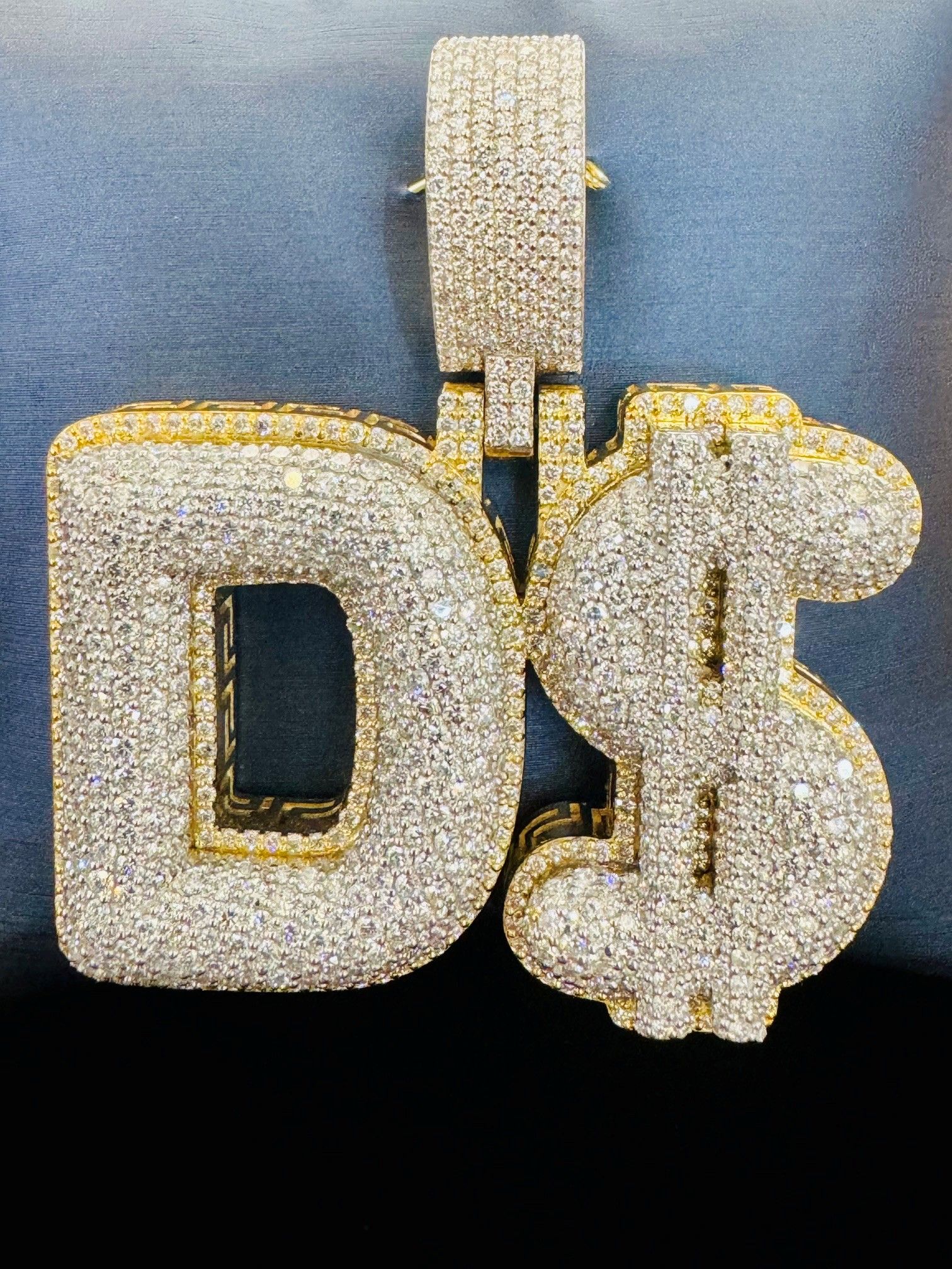 Sparkly gold and silver “D$” pendant necklace on a black background