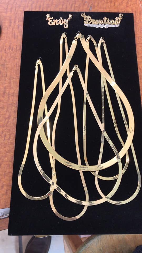 Black display board with several gold-colored necklaces arranged in loops and two small gold labels at the top