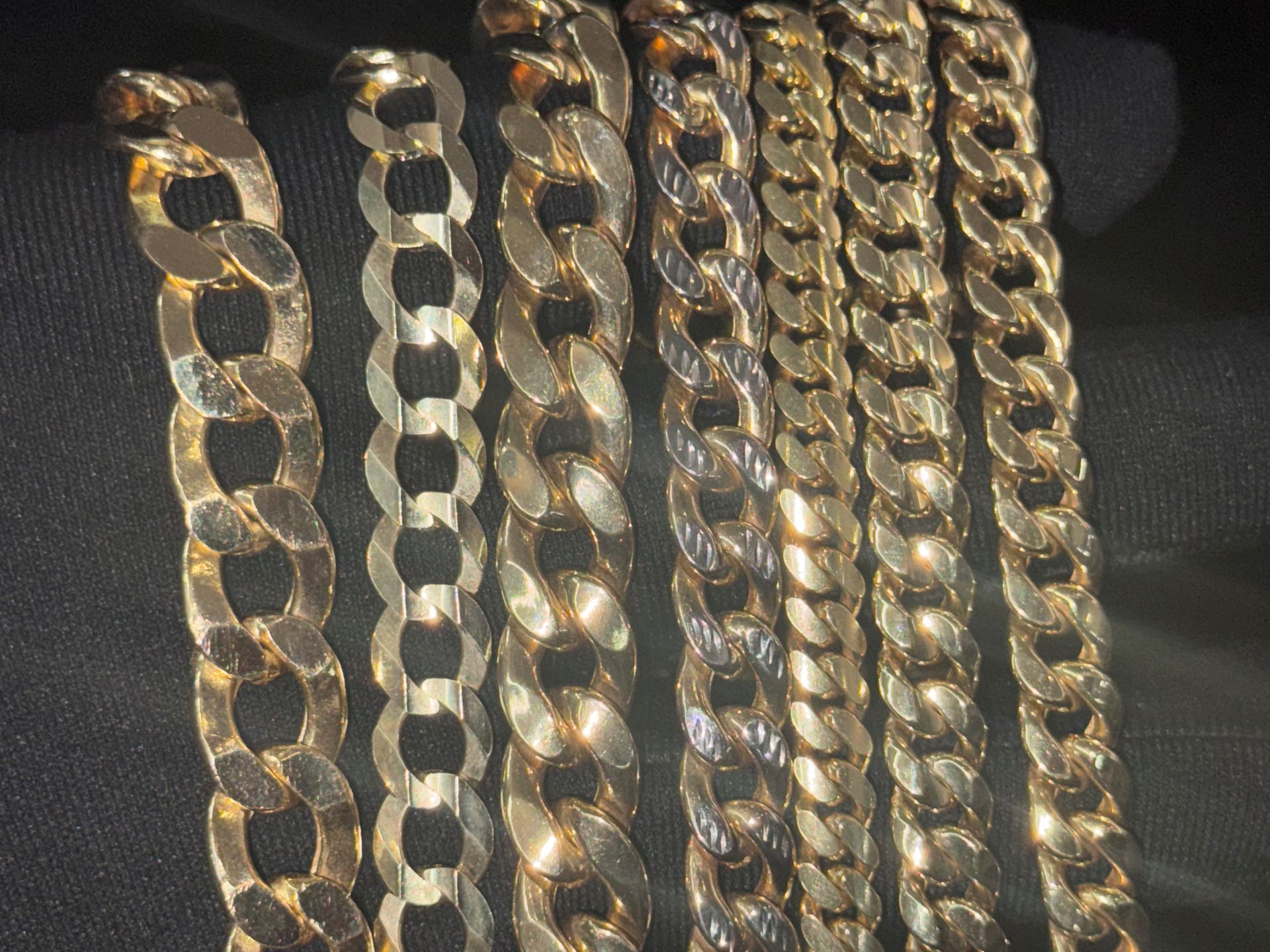 Assorted gold and silver chain necklaces laid out vertically on a dark background