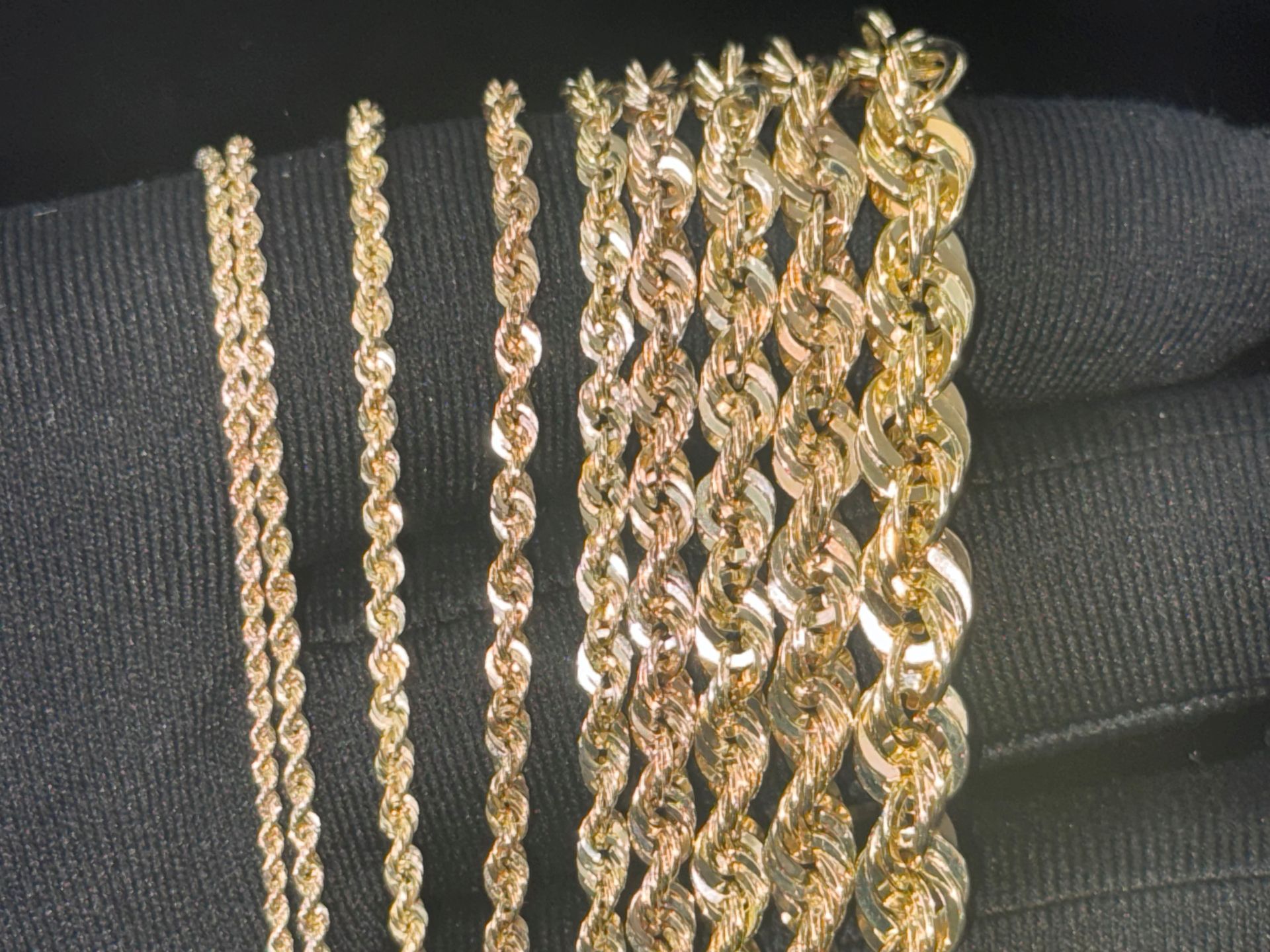 Gold necklaces and chains arranged vertically on a black fabric background