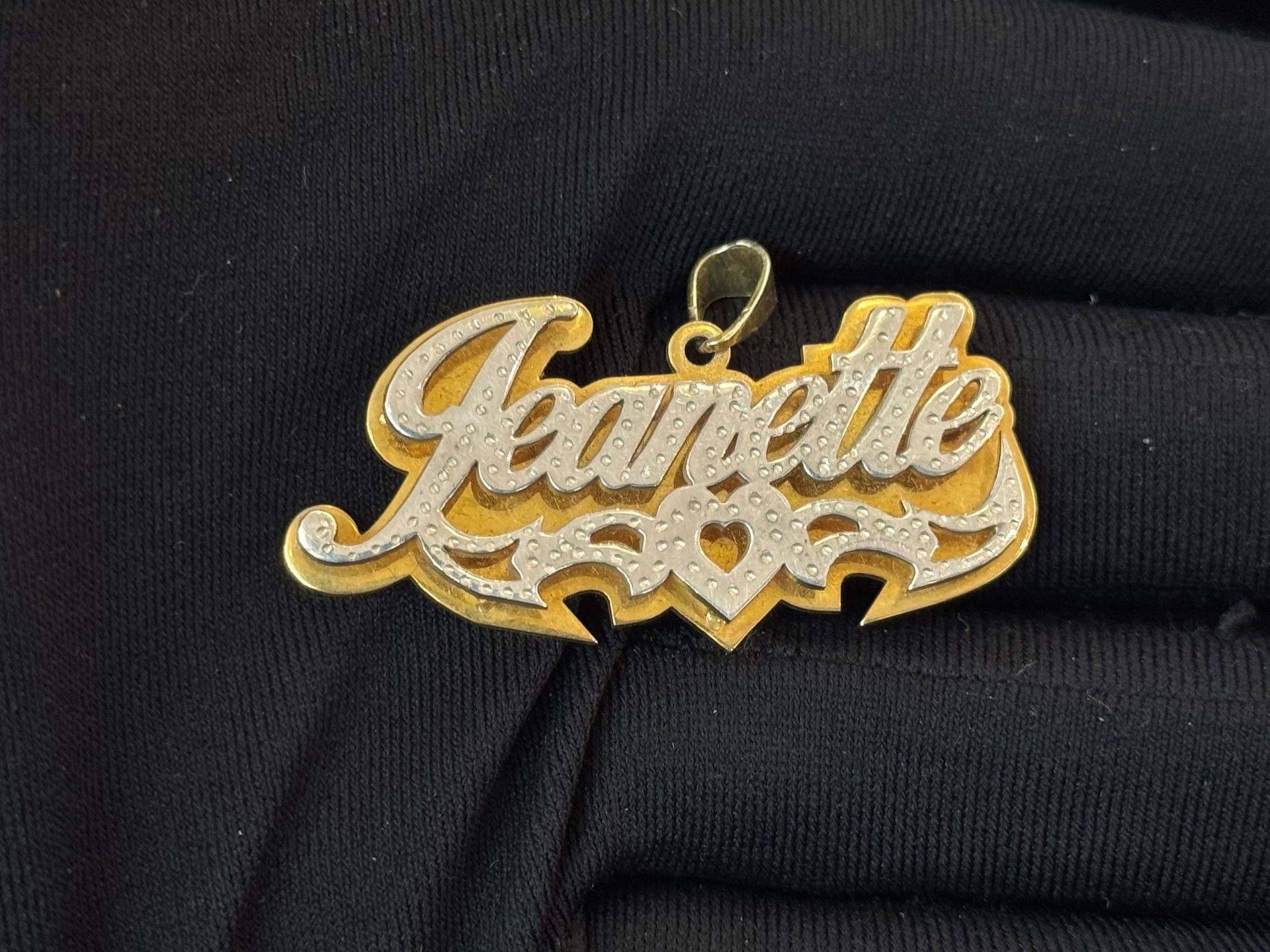 Gold “Jeanette” name pendant on a black fabric background