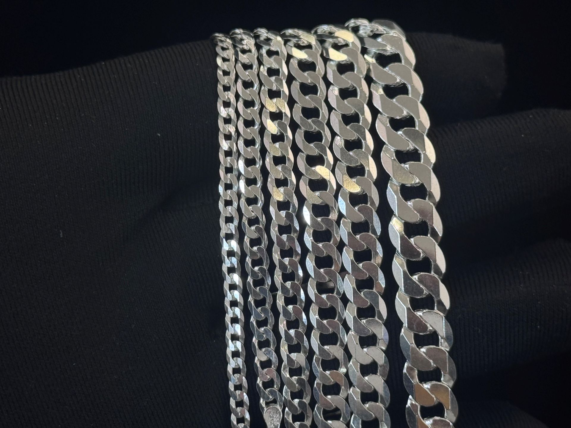 Silver chain necklaces draped over dark fabric, showing several different link styles