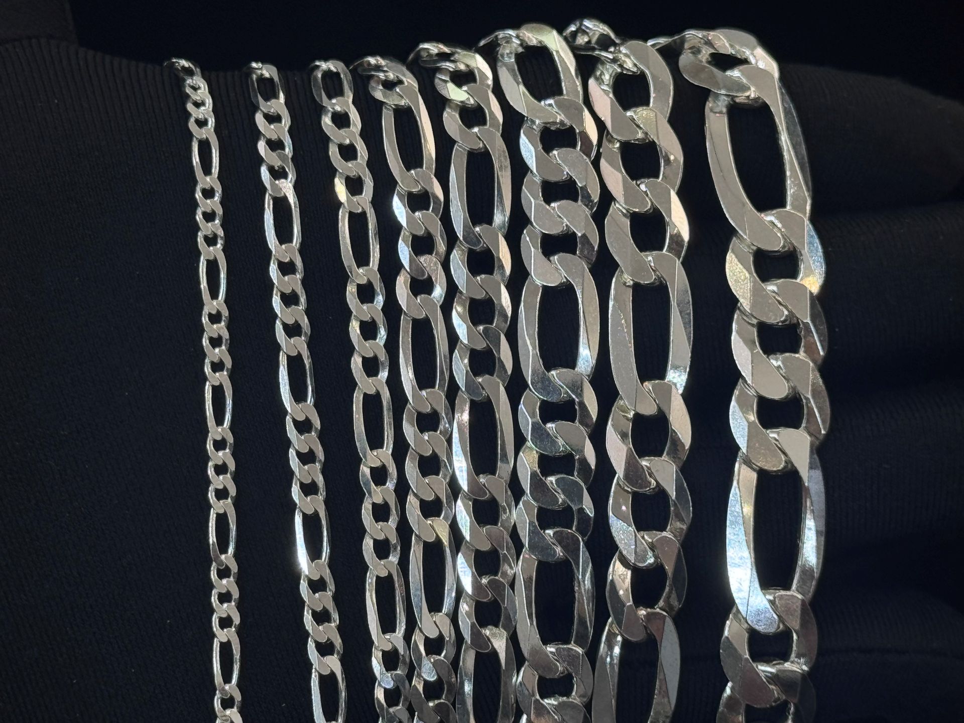 Assorted silver chain necklaces hanging vertically against a dark background