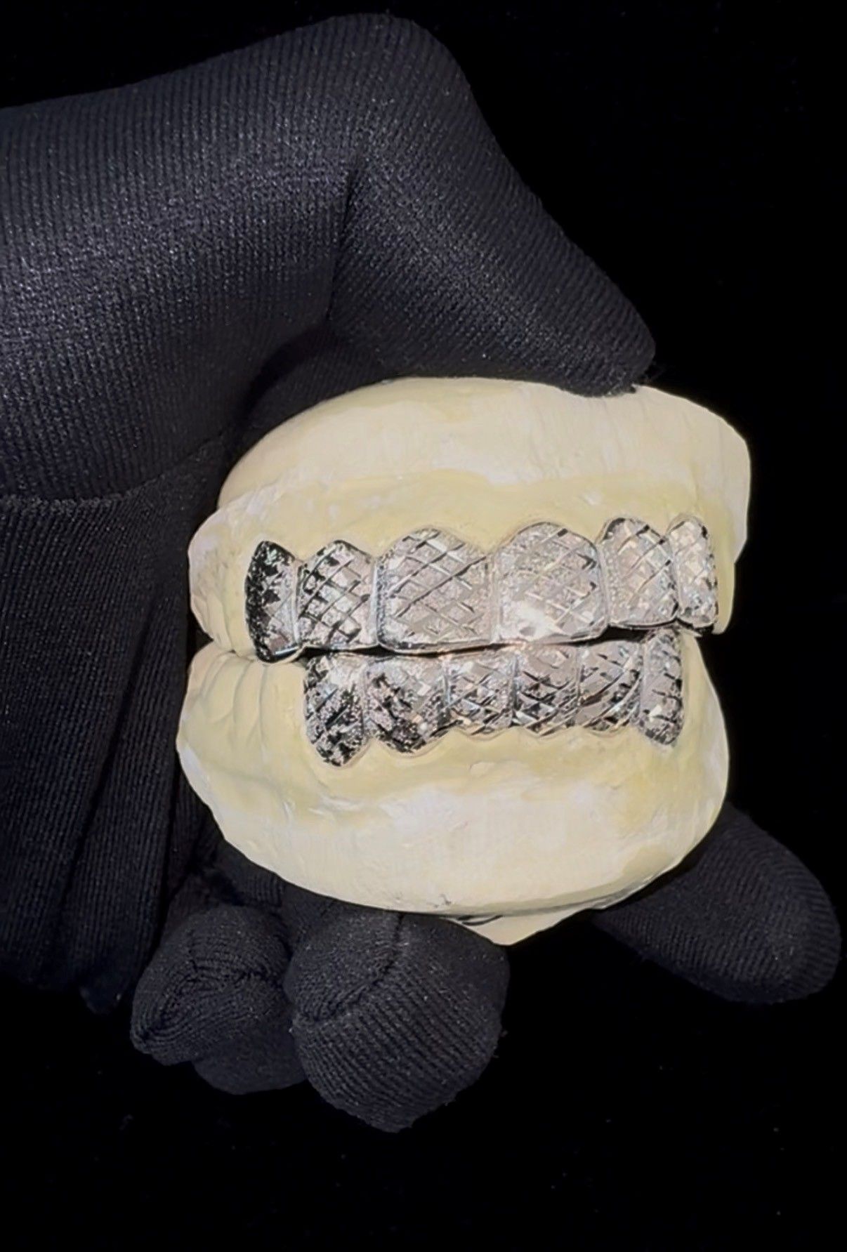 Close-up of a model of lower teeth with silver grillz held in a black-gloved hand.