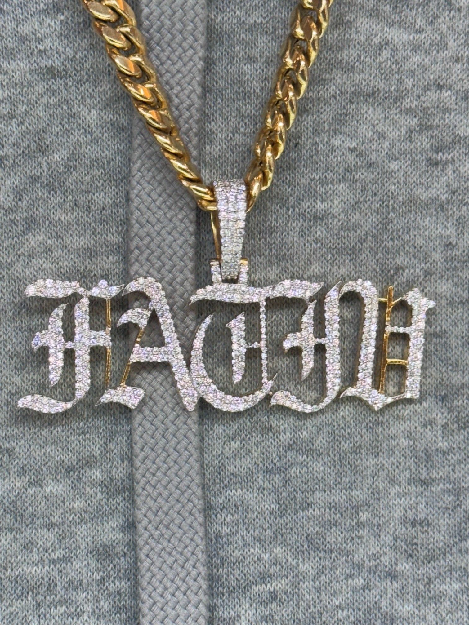 Silver “FATHA” pendant on a gold chain over a gray sweater.