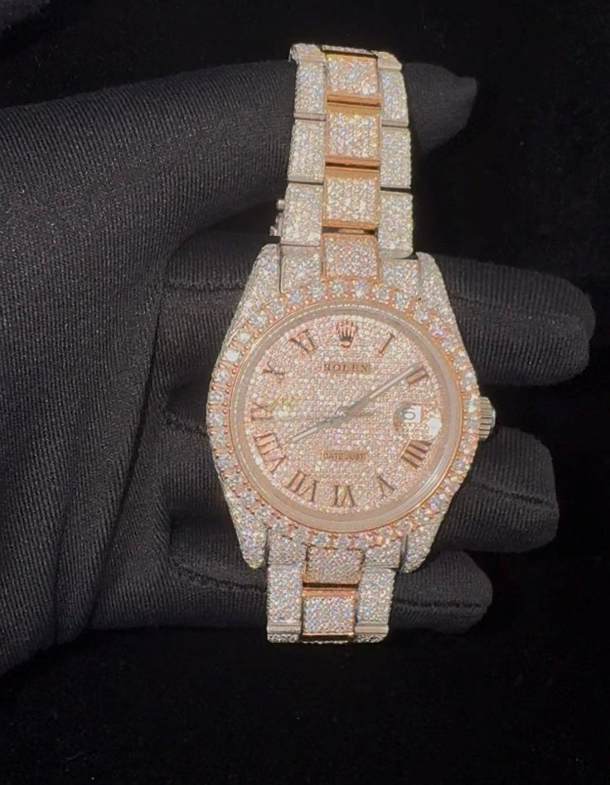 Rose gold and diamond-encrusted wristwatch held in a black-gloved hand on a dark background