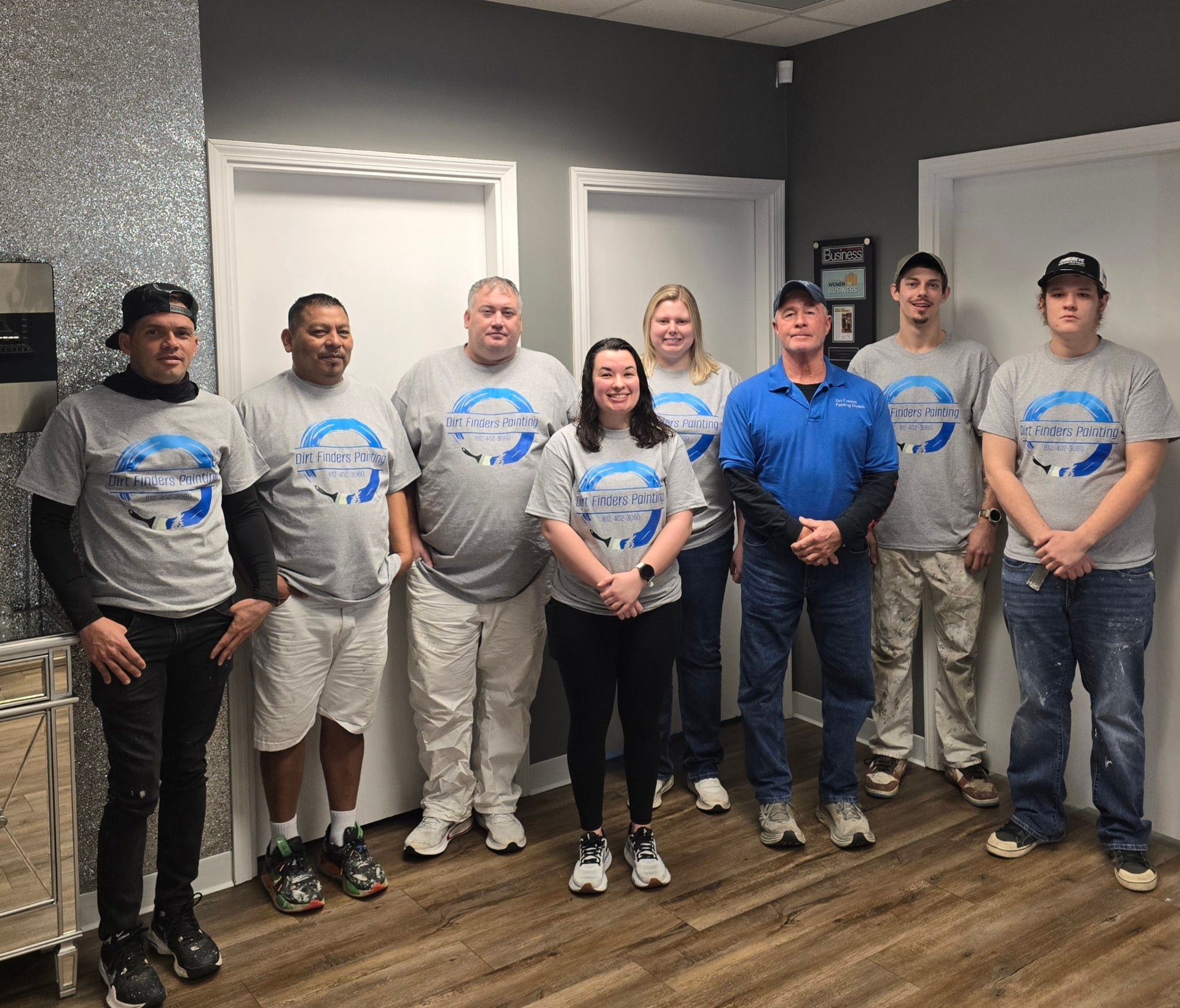 Group of people in matching shirts posing in an office. Some are smiling, and one person is wearing a blue shirt. 