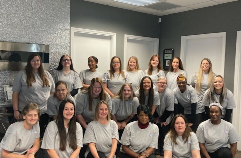 Group of women in gray shirts posing in an office setting.