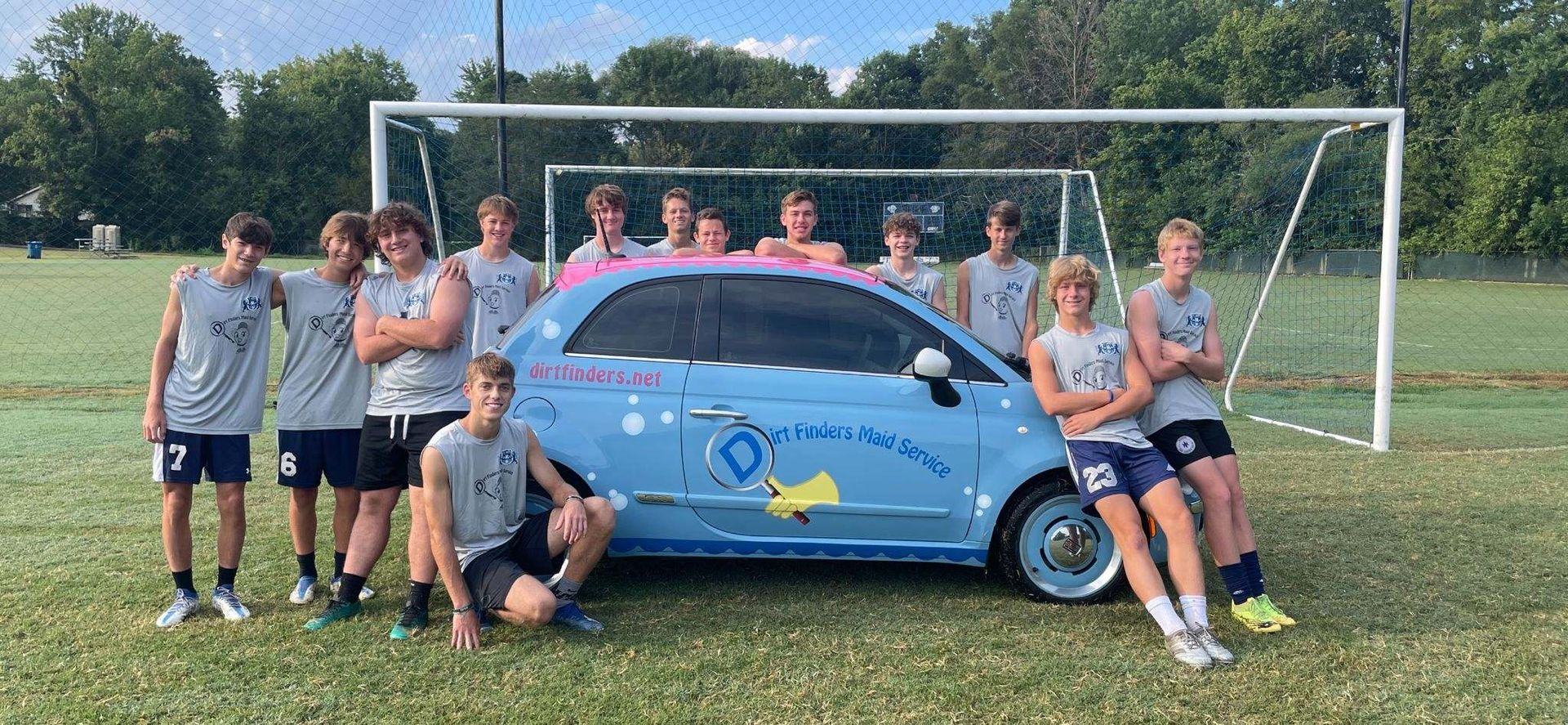 A group of young men are posing for a picture in front of a blue car.