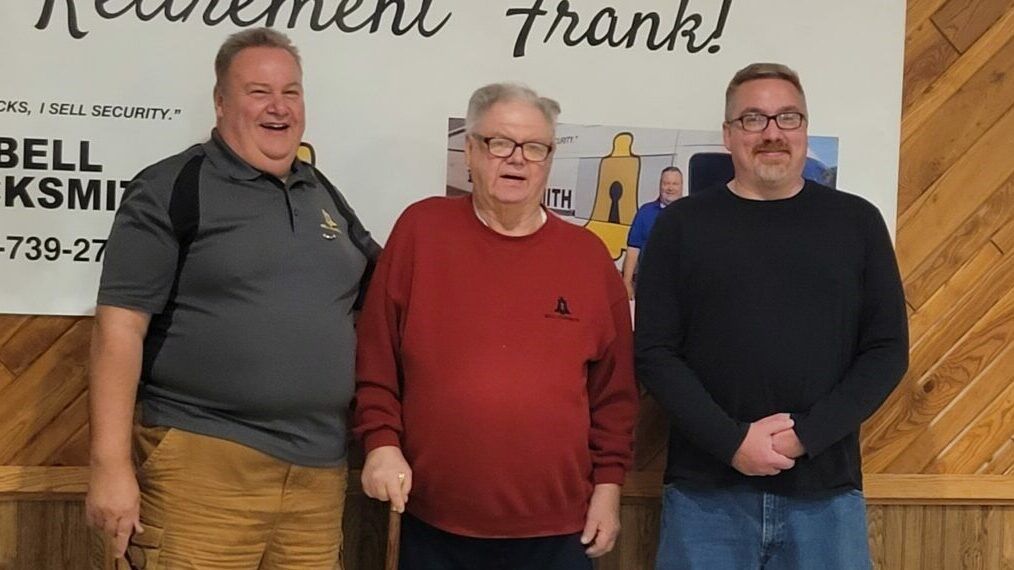 Three men are standing in front of a sign.