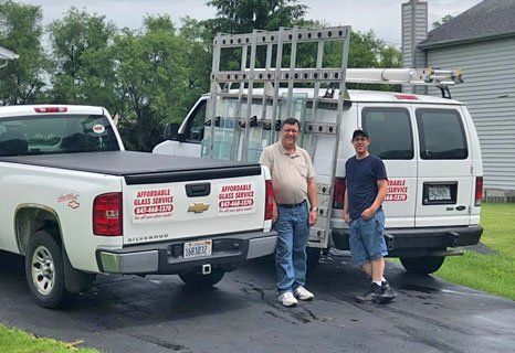 Two men standing beside Affordable Glass Service trucks