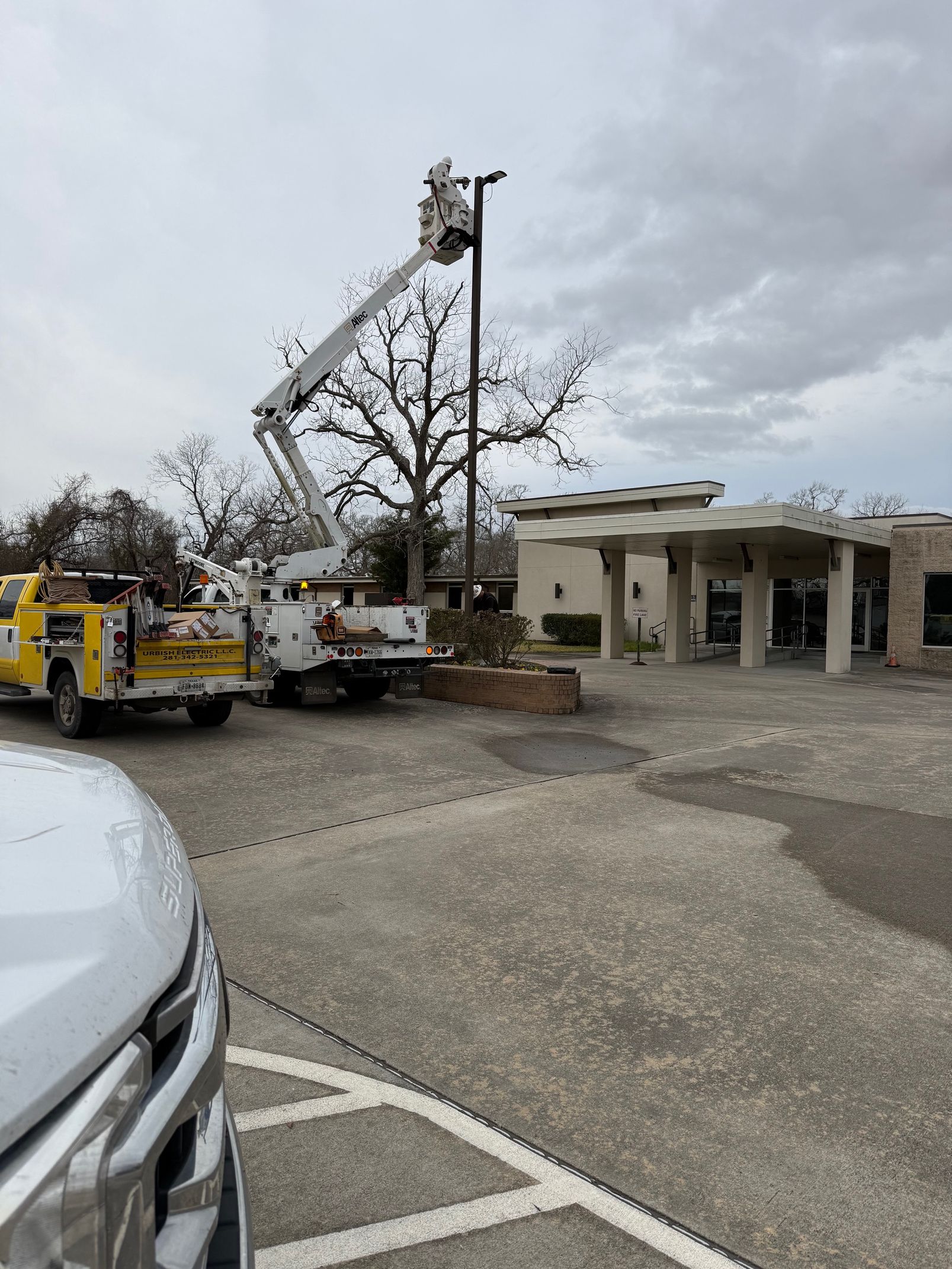 A utility truck with an extended boom lift performs maintenance on a tall outdoor light pole in a parking lot.