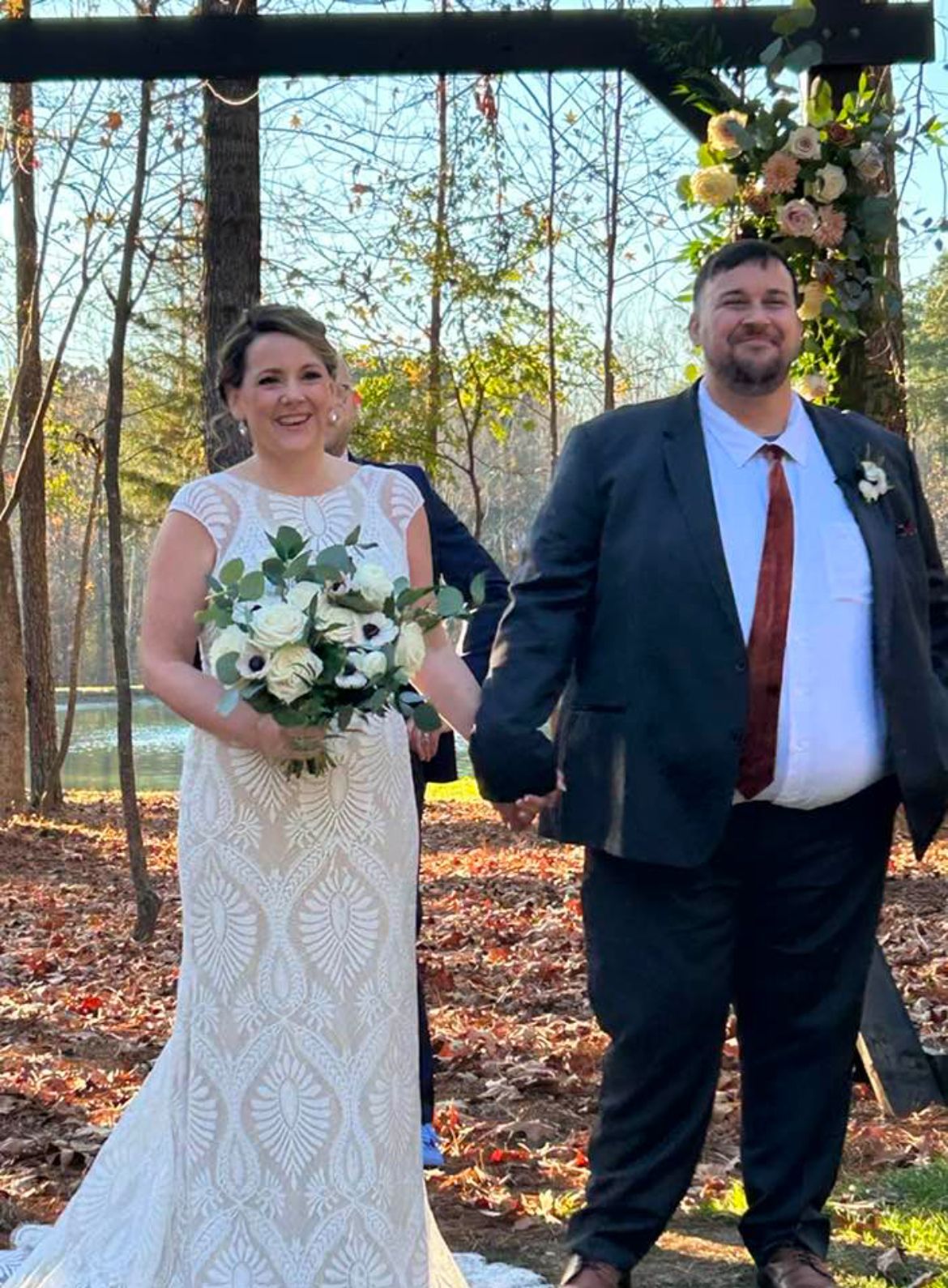 Bride and groom holding hands, standing near floral archway during outdoor wedding.