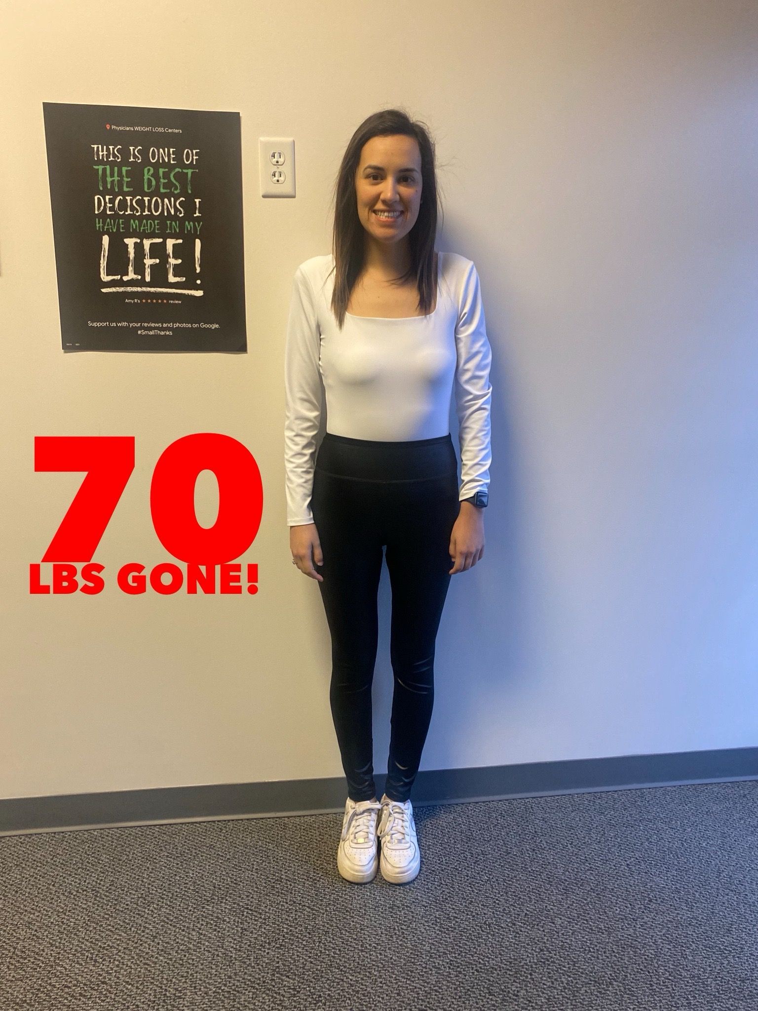Woman in white top and black pants stands in front of a wall with a sign. Text says 
