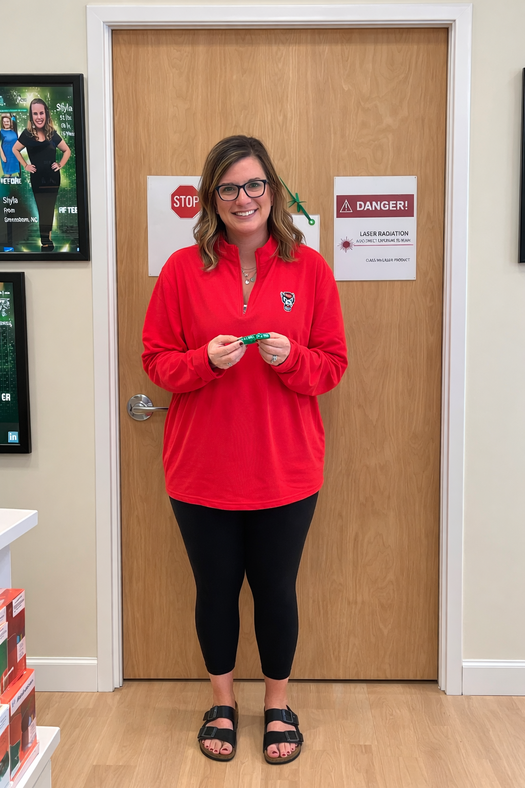 Woman in red sweater and black leggings stands in a doorway, holding a small object.