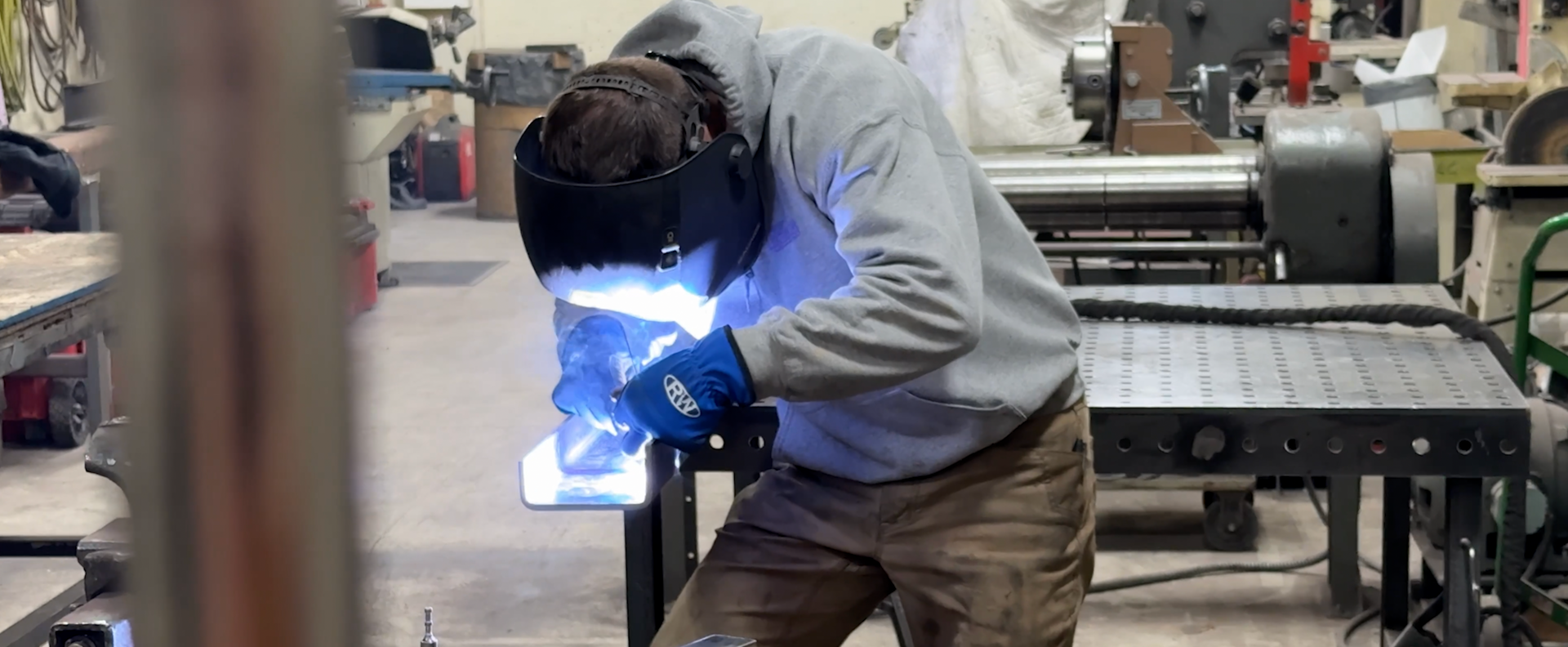 A person welding metal in a workshop, wearing a protective helmet and gloves.