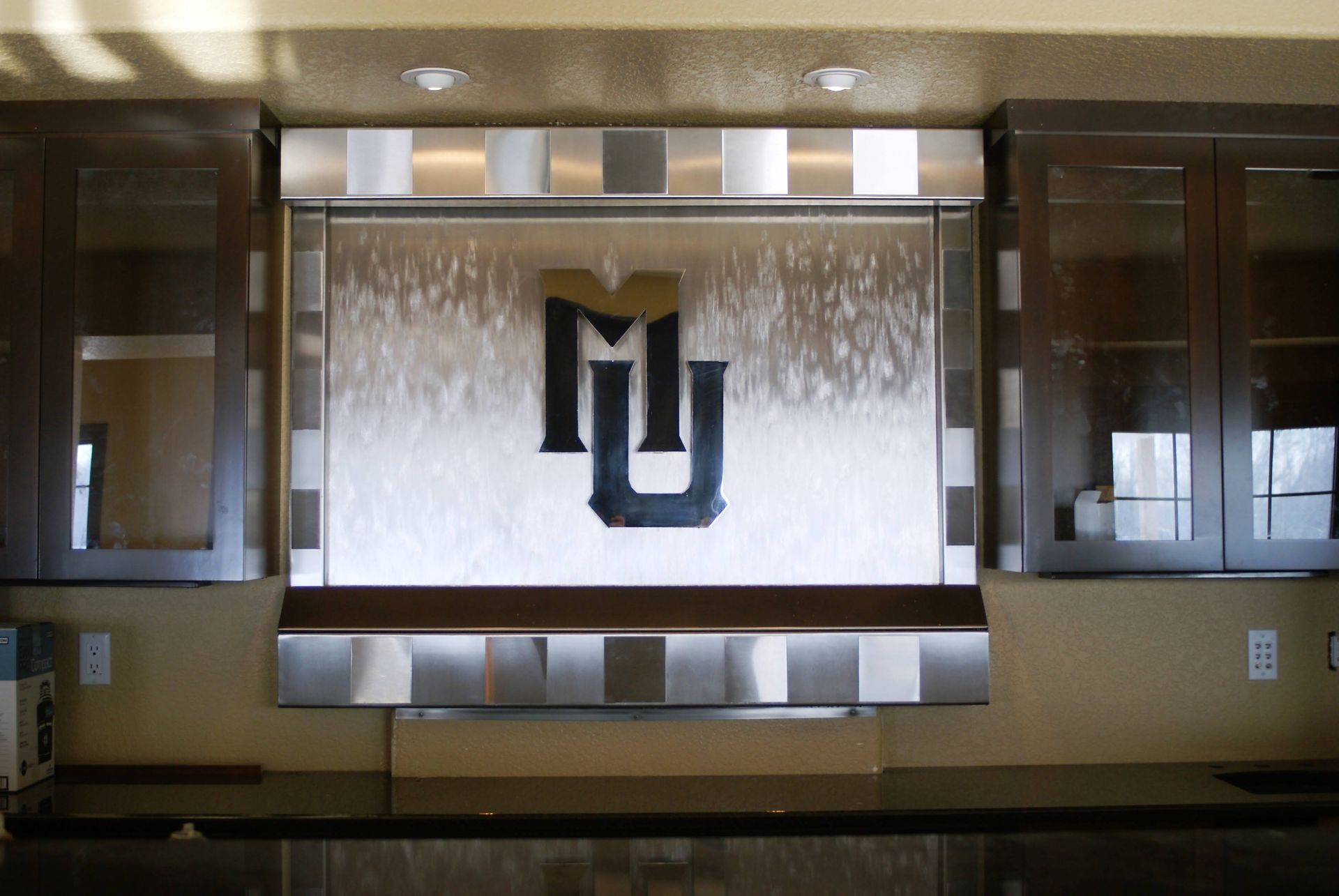 Water feature with a university logo centered between metal cabinets.