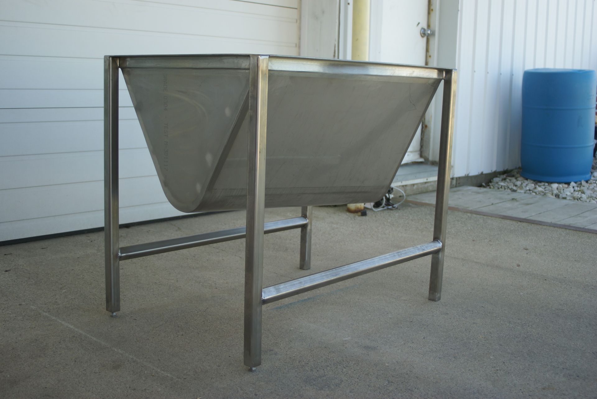 Stainless steel angled hopper on legs, outdoors.
