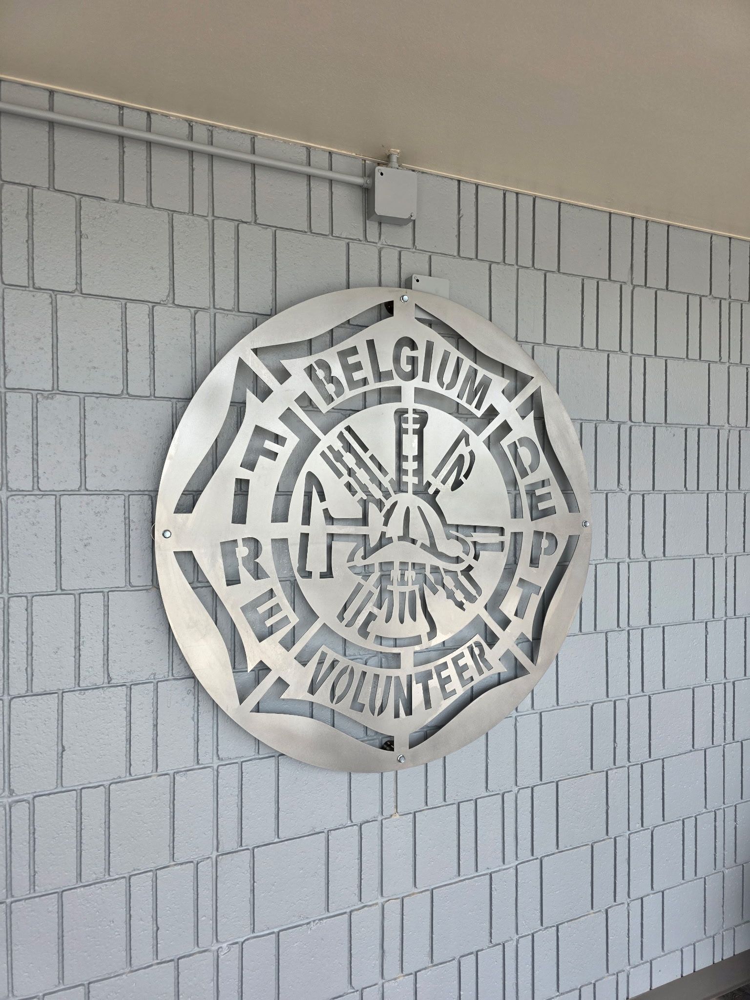 Metal sign of Belgium Fire Department logo on brick wall.