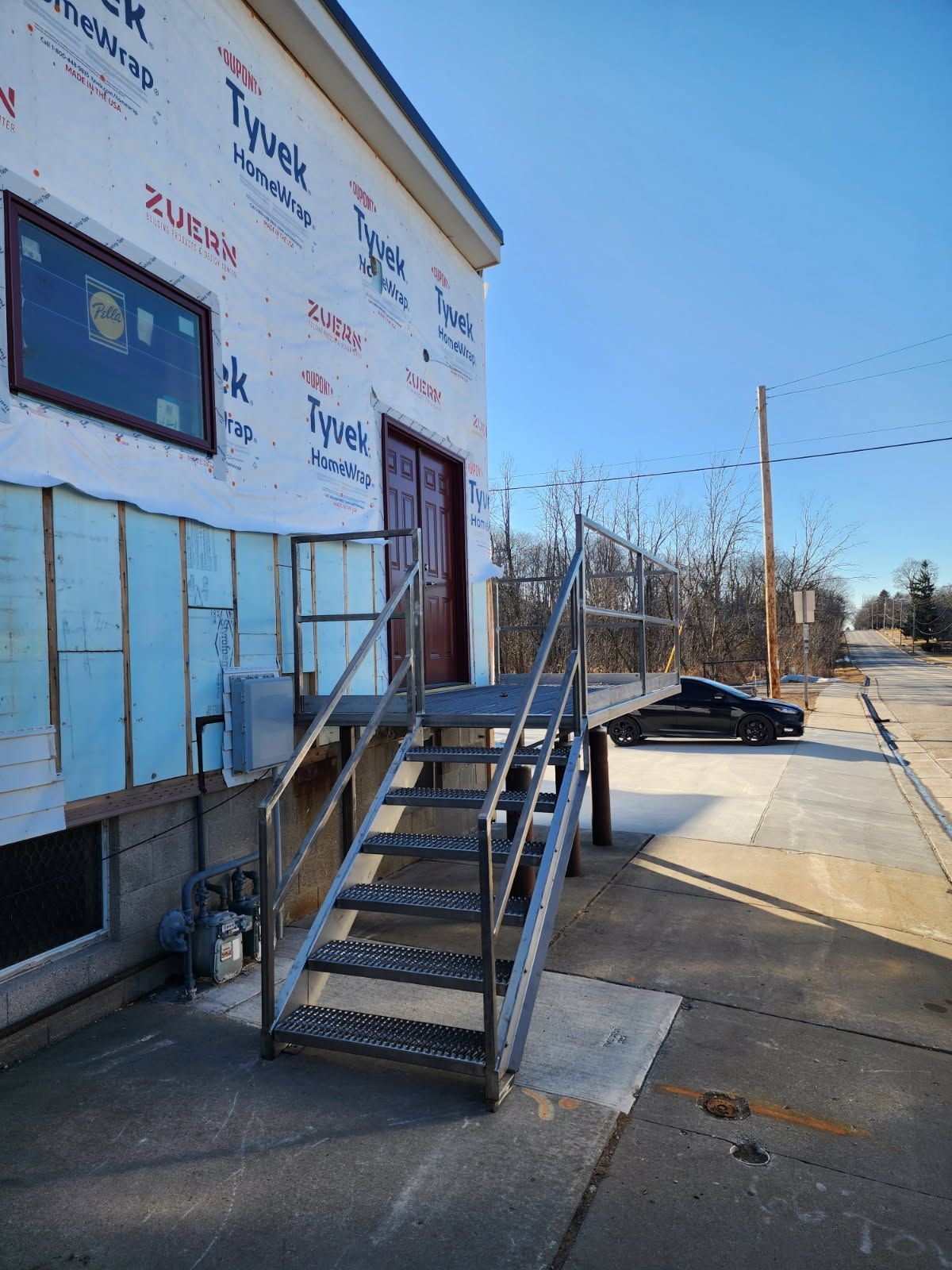 Exterior building with metal stairs, door, and Tyvek wrap on a sunny day.