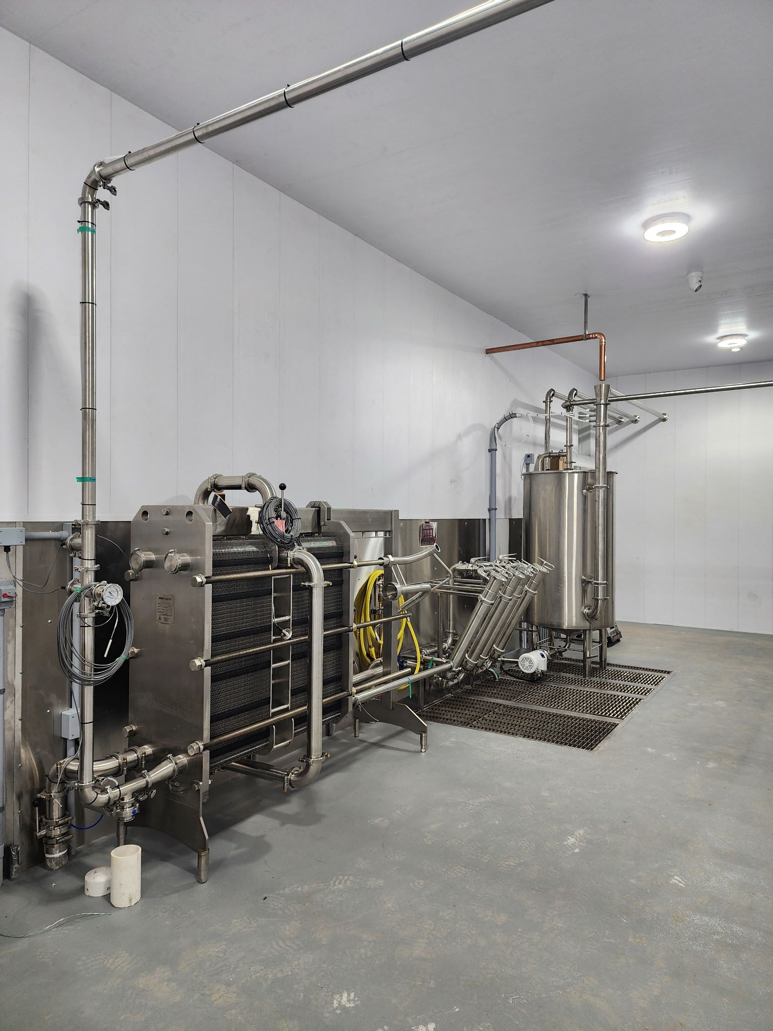 Stainless steel industrial dairy processing equipment in a white room.