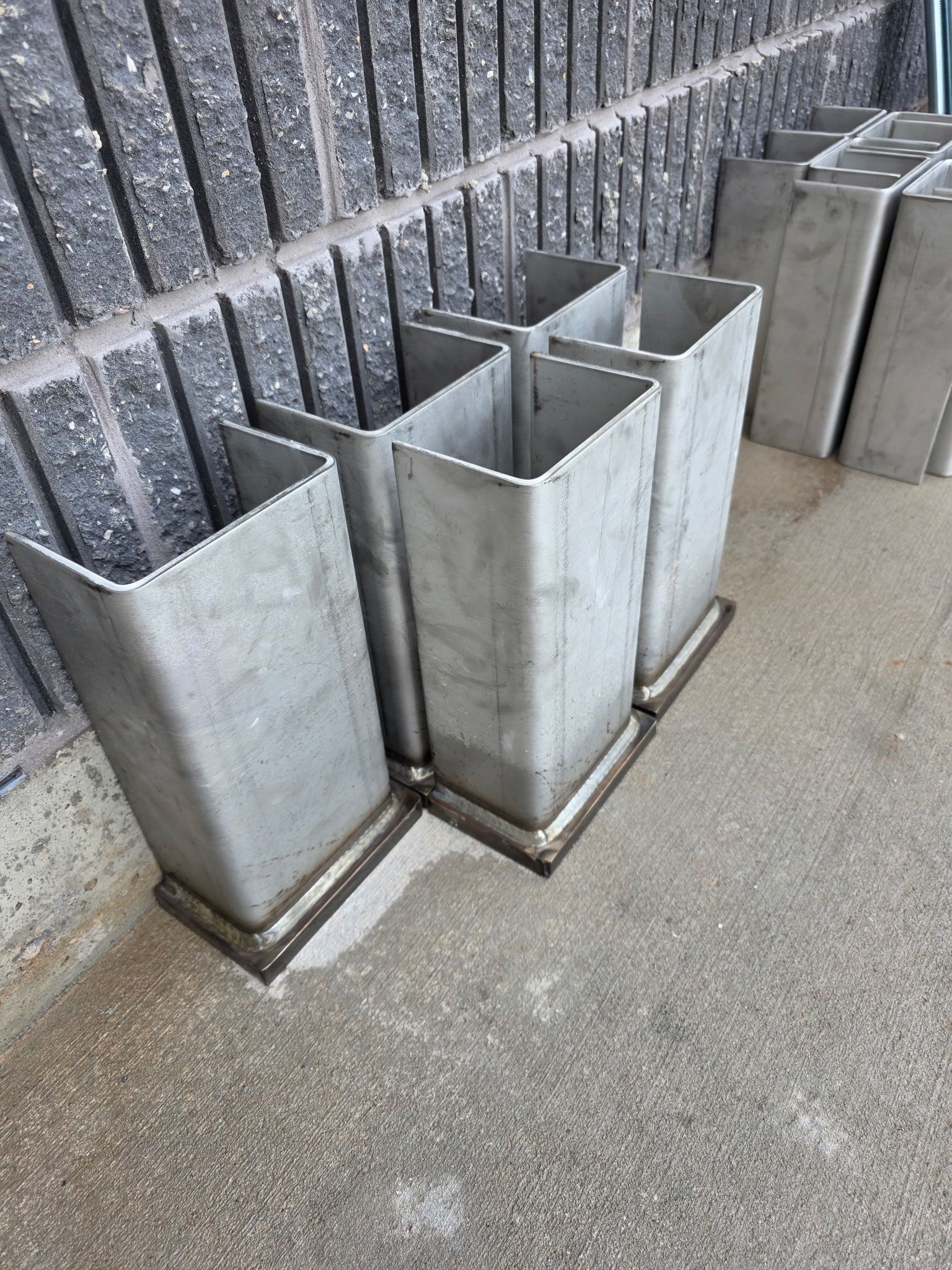 Six gray rectangular metal columns set against a textured brick wall.