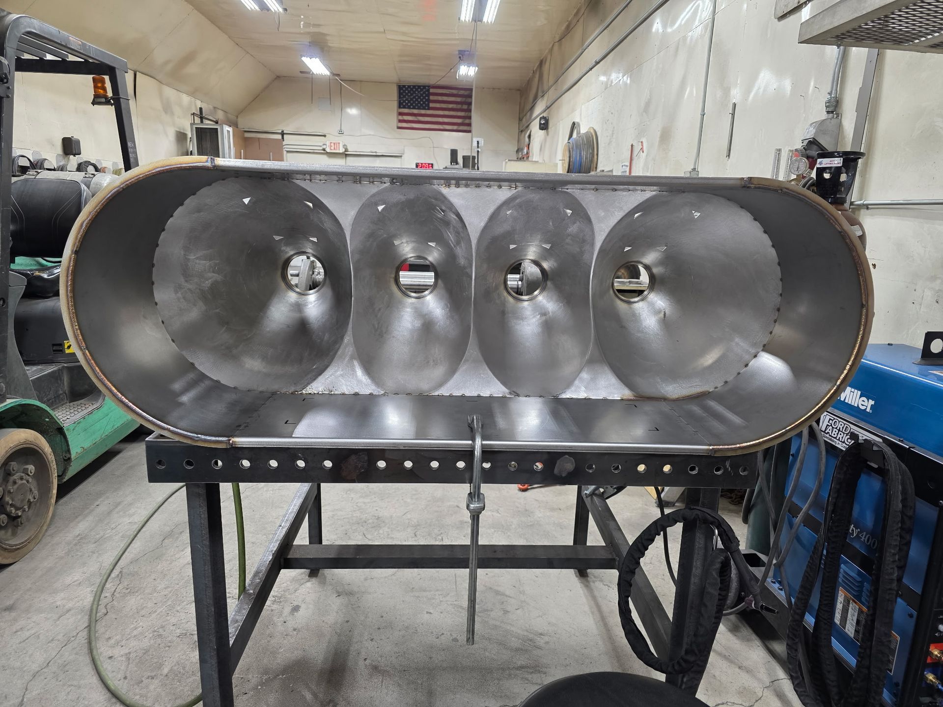 Cross-section of a metal tank with four conical chambers, sitting on a black table. Workshop setting.