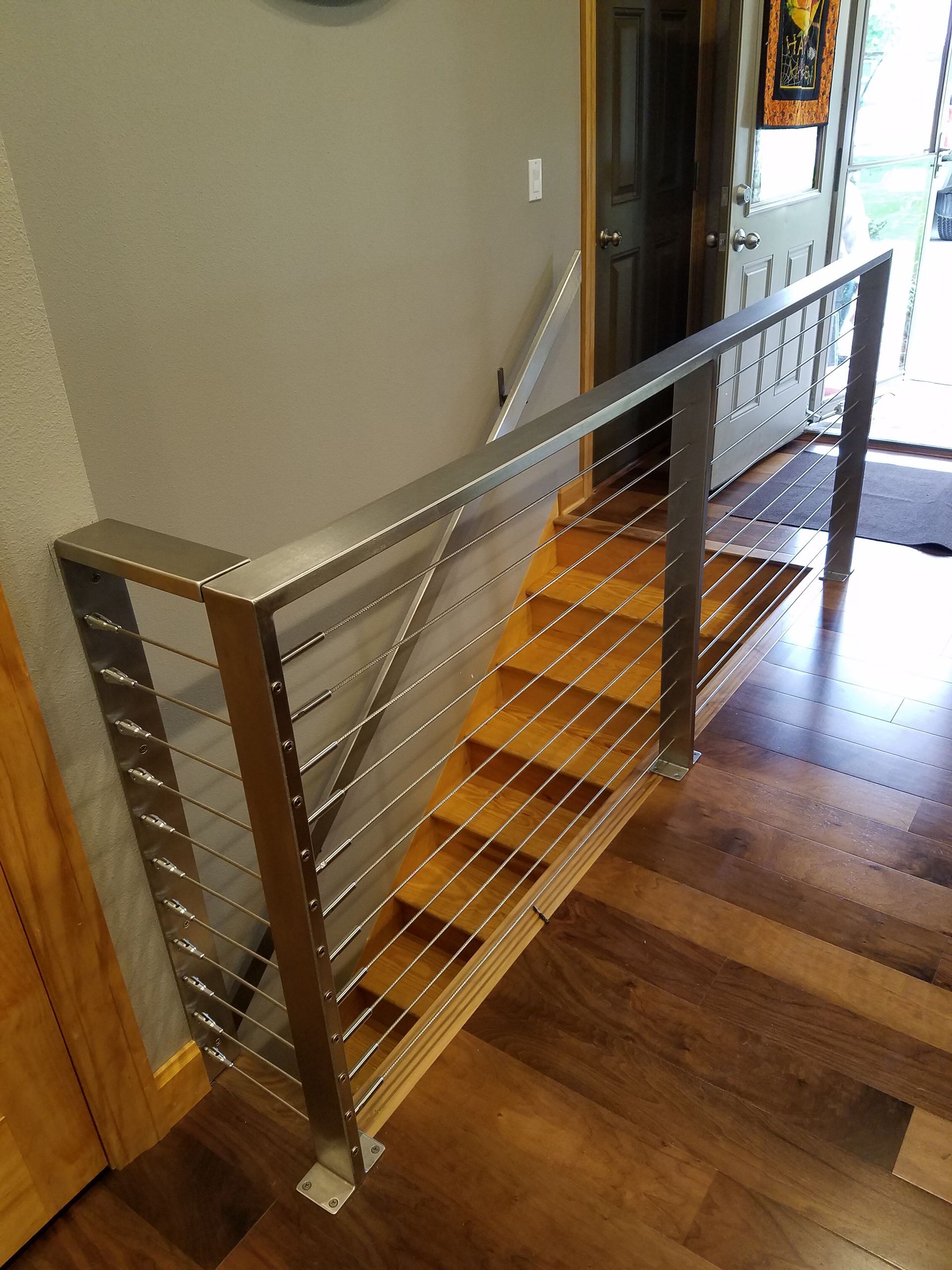 Staircase with wooden steps and stainless steel cable railing in a home setting.