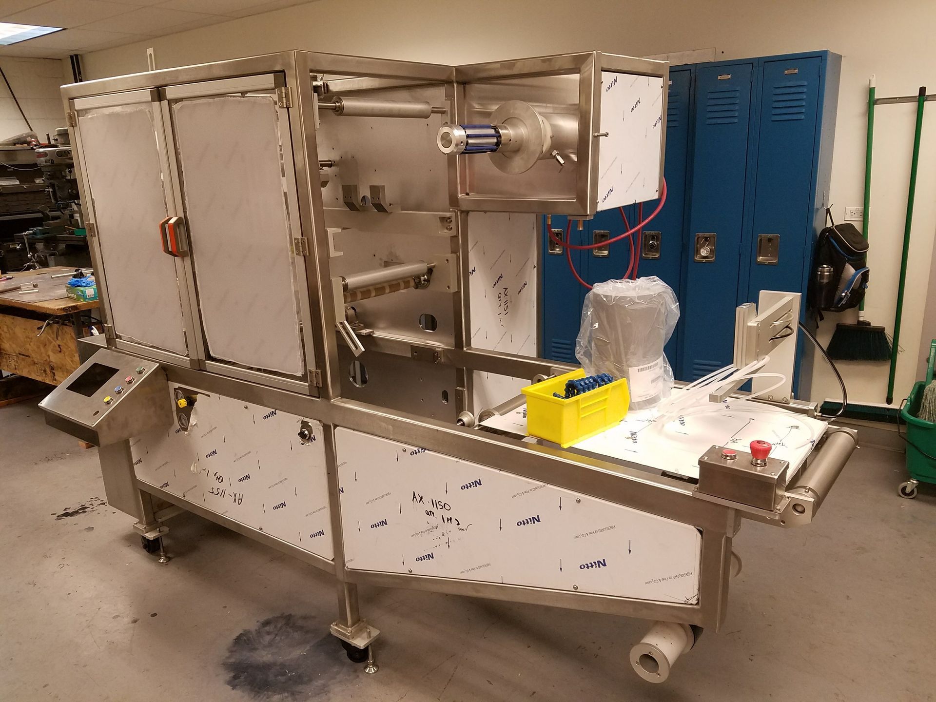 Stainless steel industrial packaging machine with conveyor belt, in a workshop setting.