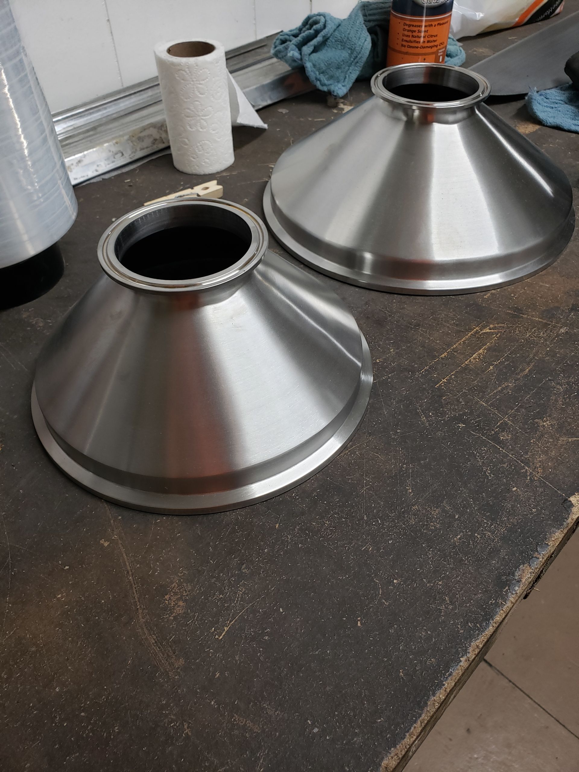 Two stainless steel cone-shaped objects, possibly funnels, on a workbench.
