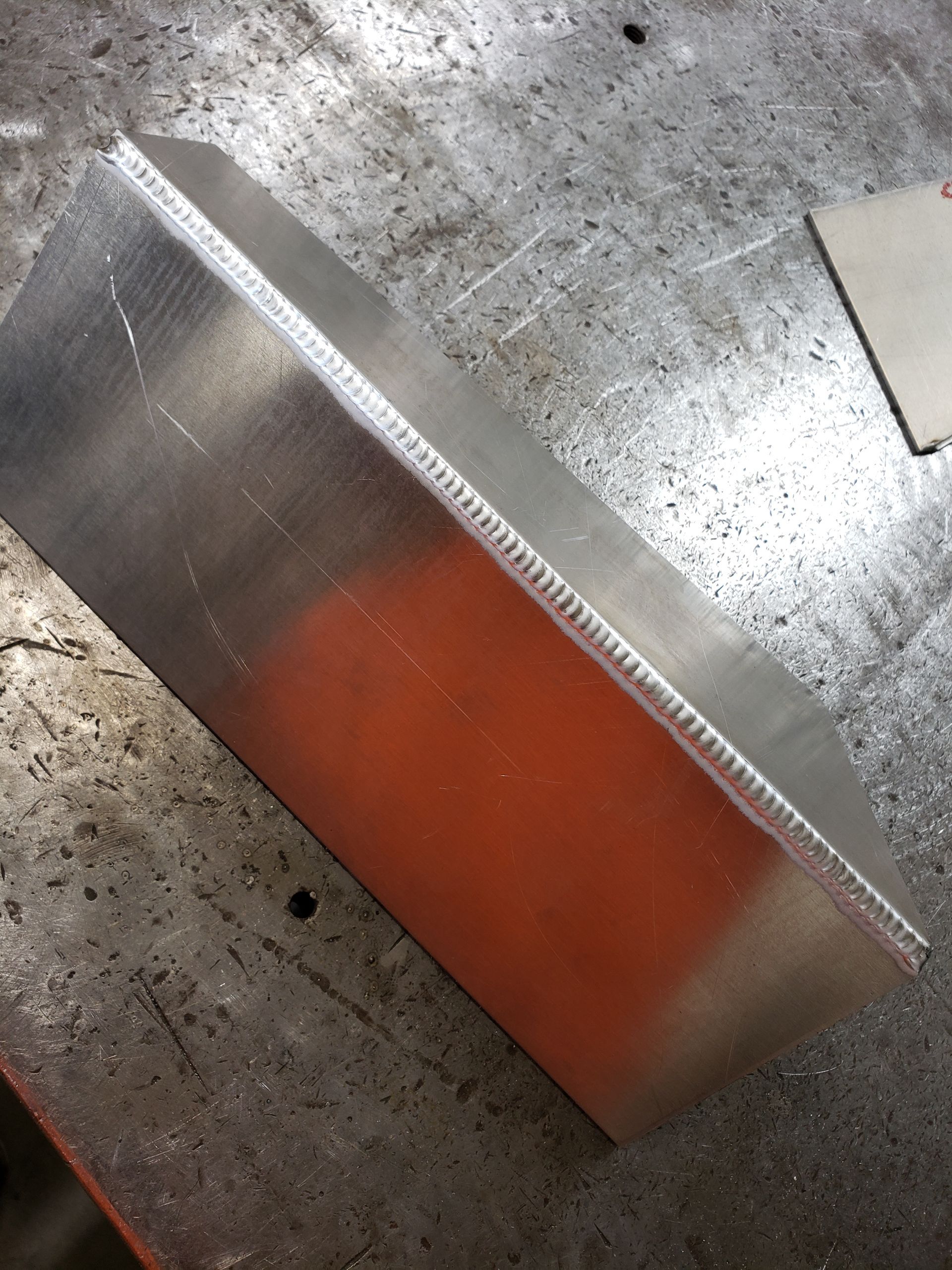 Welded aluminum box on a metal surface; a close-up shot with orange spray paint visible inside.
