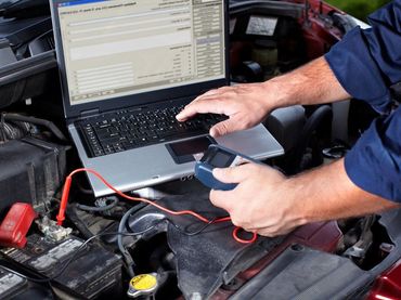 A man is working on a laptop under the hood of a car.