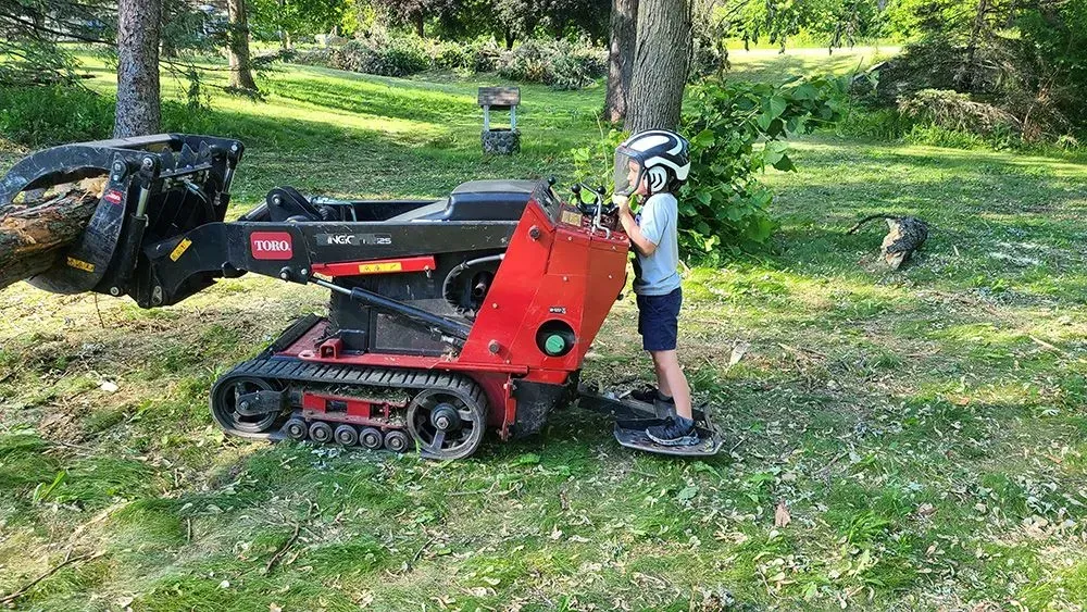 A young boy is standing next to a small tractor in a park.